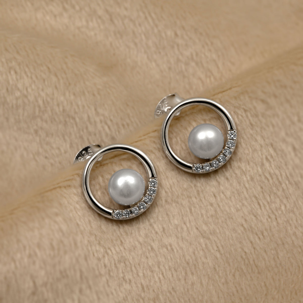 Pearl and silver circular earrings with lab grown diamonds on a beige fabric background