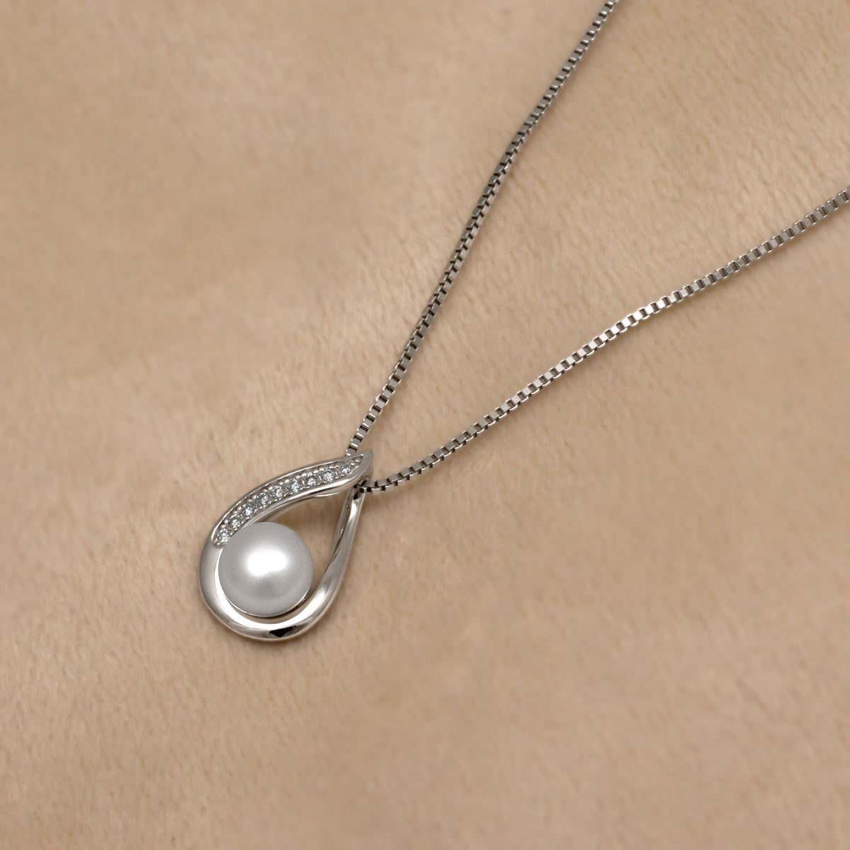 Silver necklace with a teardrop-shaped pendant featuring a pearl on a beige background