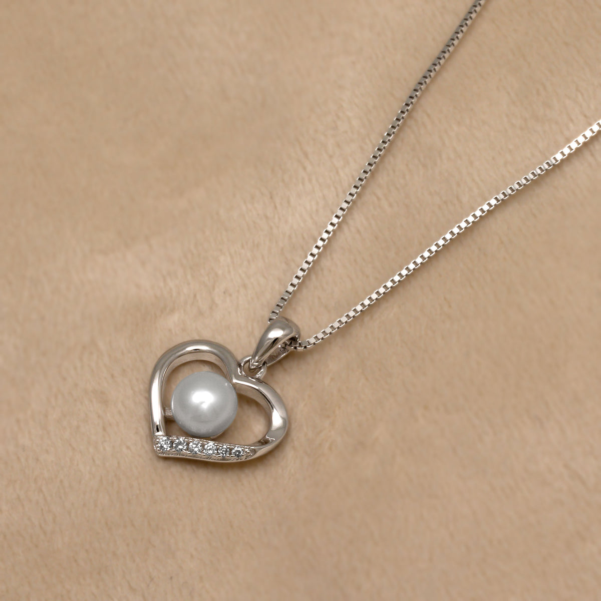 Silver necklace with a heart-shaped pendant featuring a pearl and lab grown diamonds on a beige background