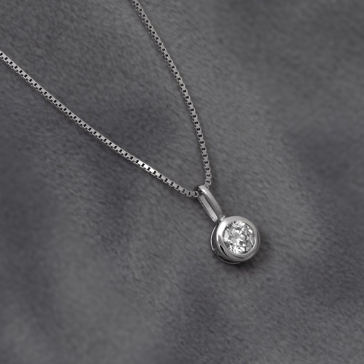 A silver box chain necklace with a round bezel-set 1/2 carat lab diamond pendant, shown against a plain grey background.