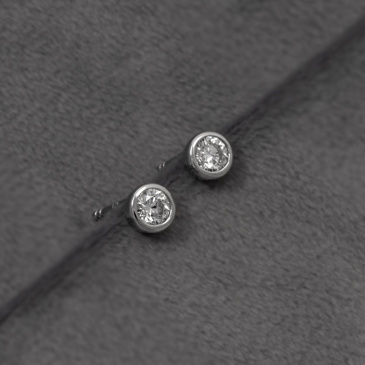 A pair of round bezel-set lab diamond stud earrings in sterling silver, shown on a plain grey background.