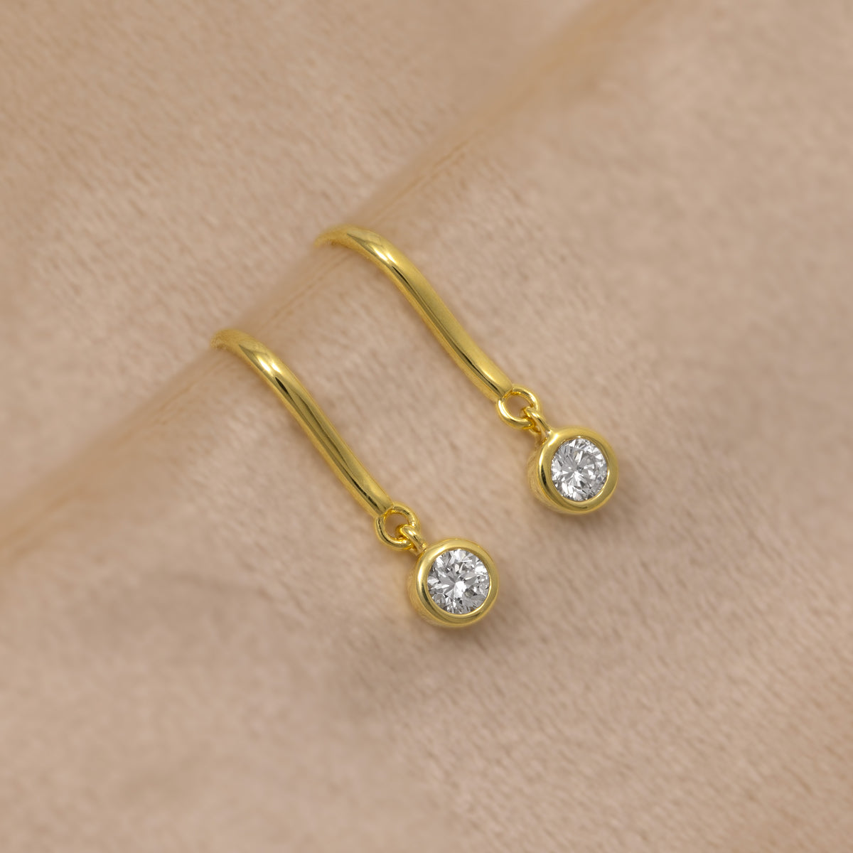 A pair of gold vermeil hook drop earrings, each featuring a quarter carat diamond, shown against a soft beige background.