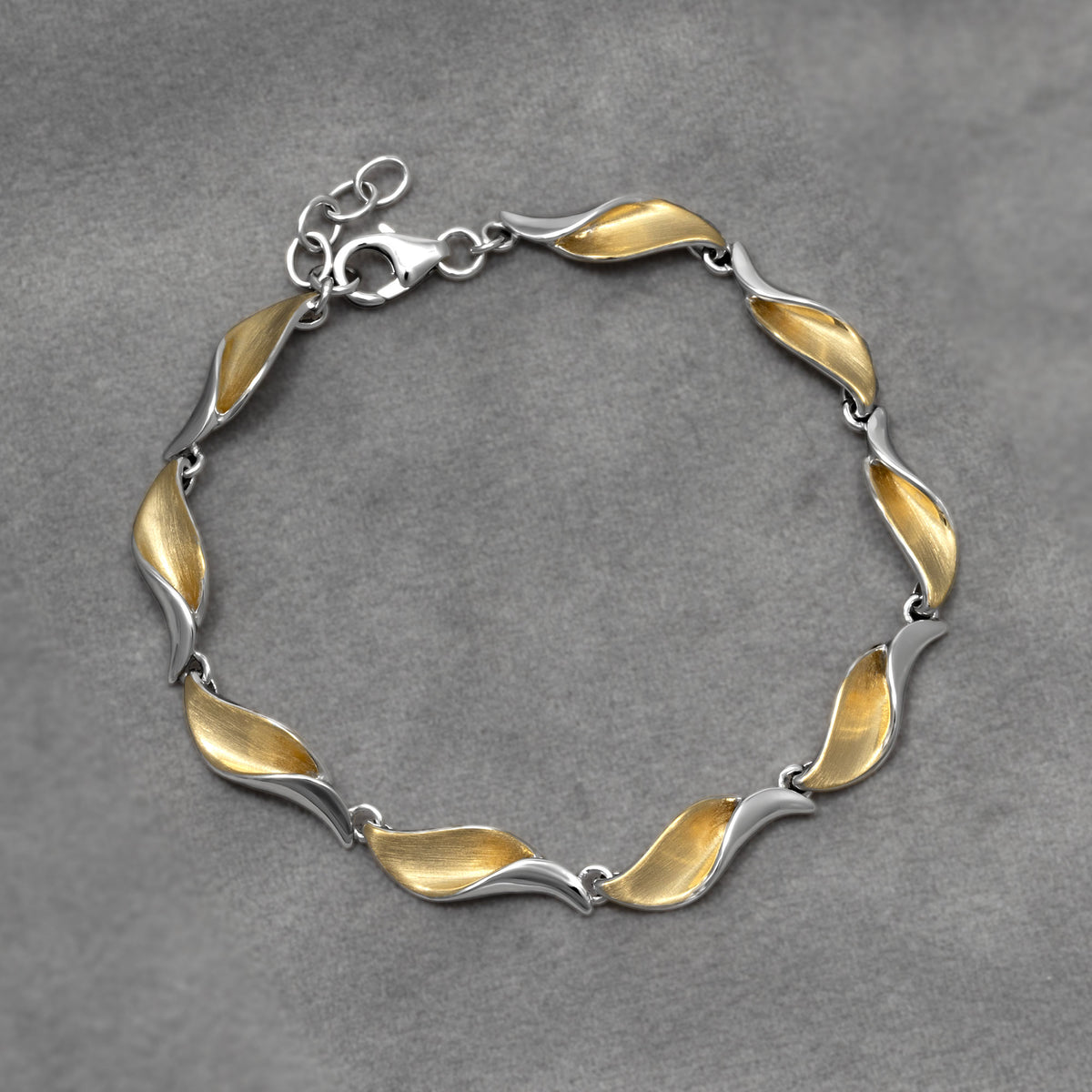 A two-tone link bracelet with a wavy, leaf-like design, featuring a satin gold vermeil finish on one side and a polished silver finish on the other, complete with a lobster clasp on a grey background.