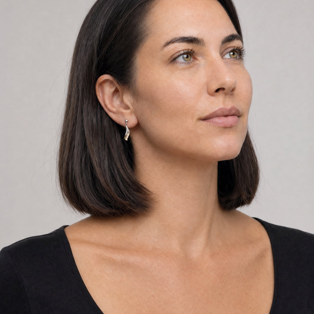 A close-up of a woman wearing a delicate gold vermeil and sterling silver drop earring, against a neutral gray background.