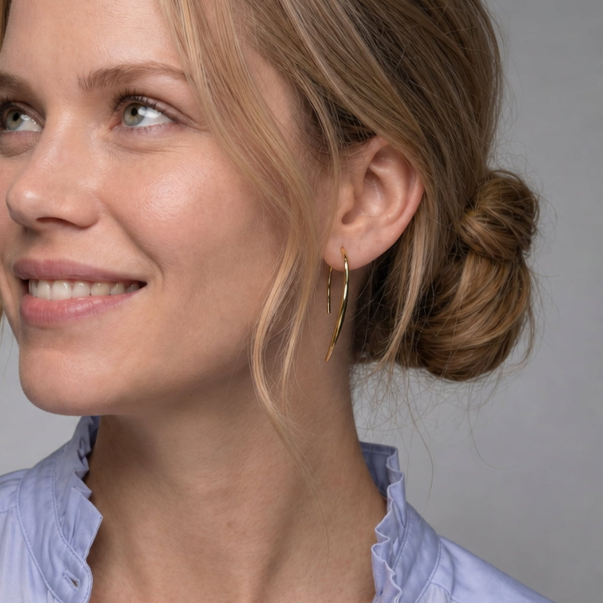 A model wears a pair of gold vermeil hook earrings with a polished finish.