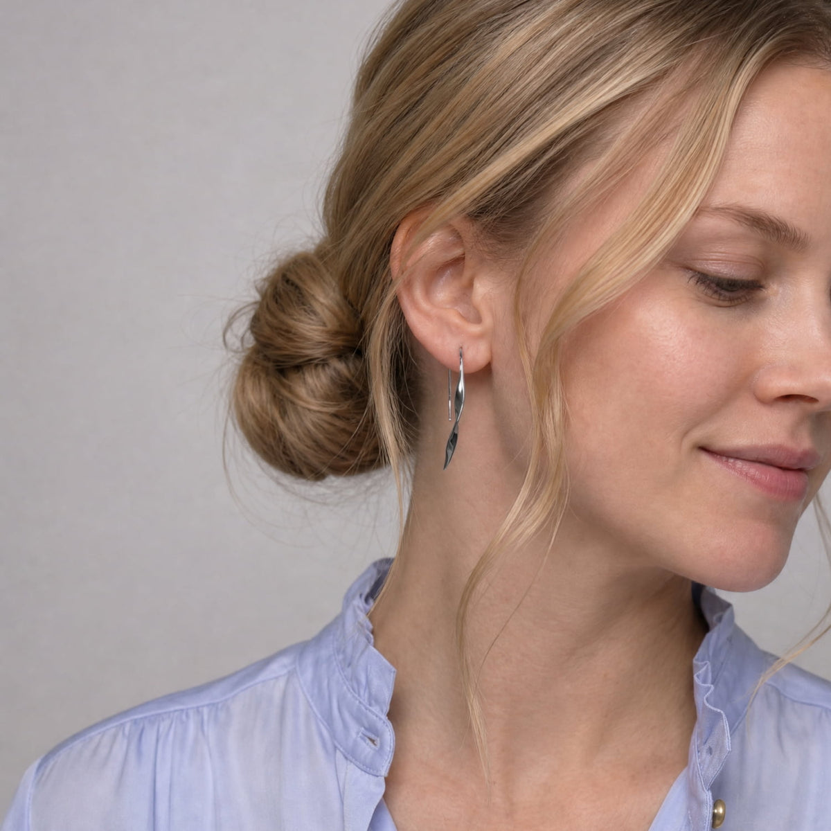 A model wears a pair of sterling silver twisting drop earrings with fishhook backs.