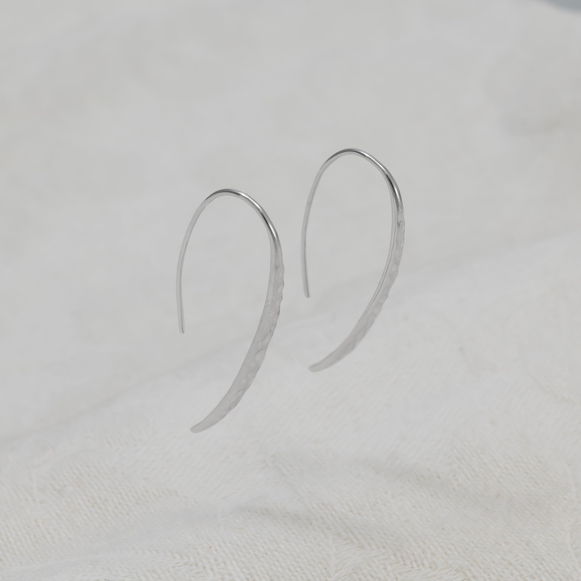 A pair of sterling silver hammered drop earrings with fishhook backs.