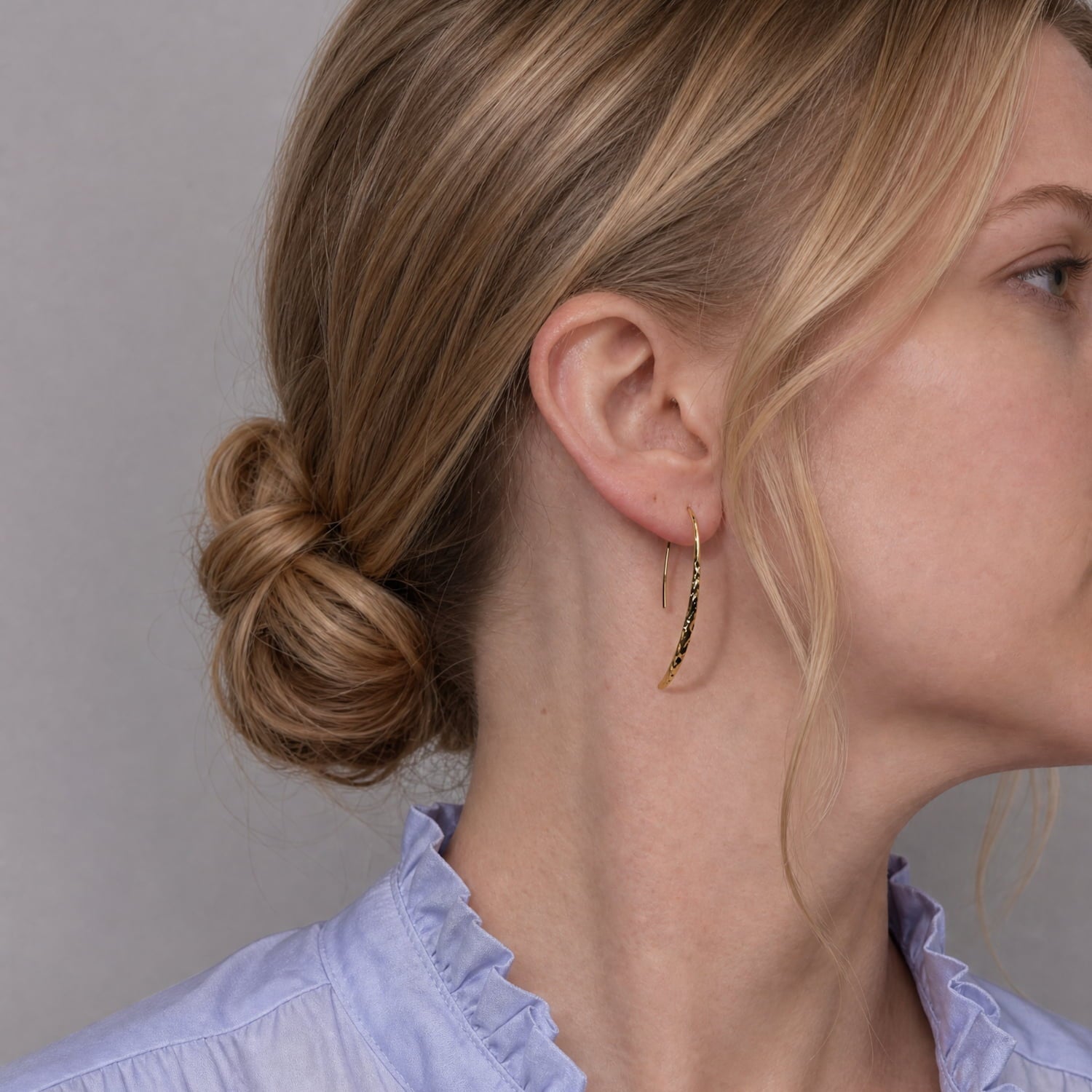 Model wears a pair of gold vermeil, hammered drop earrings with a curved, teardrop-like shape and fishhook backings.