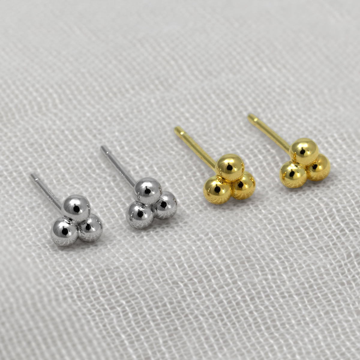 Stud earrings with clustered spherical bead designs, shown in silver and gold vermeil on a textured white fabric background.