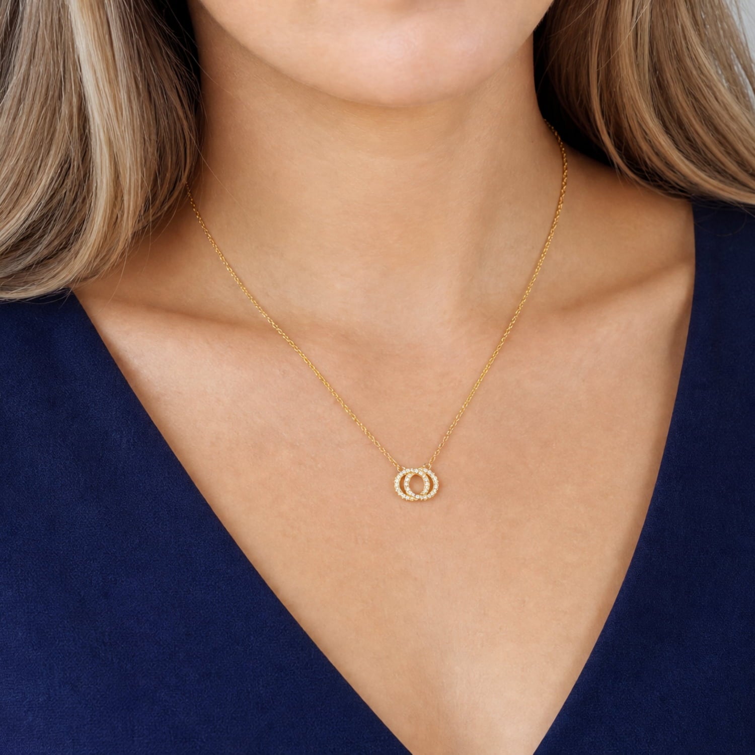 Delicate yellow gold vermeil necklace featuring two reversible interlocking circles suspended from a fine chain, styled against a navy v-neck top.