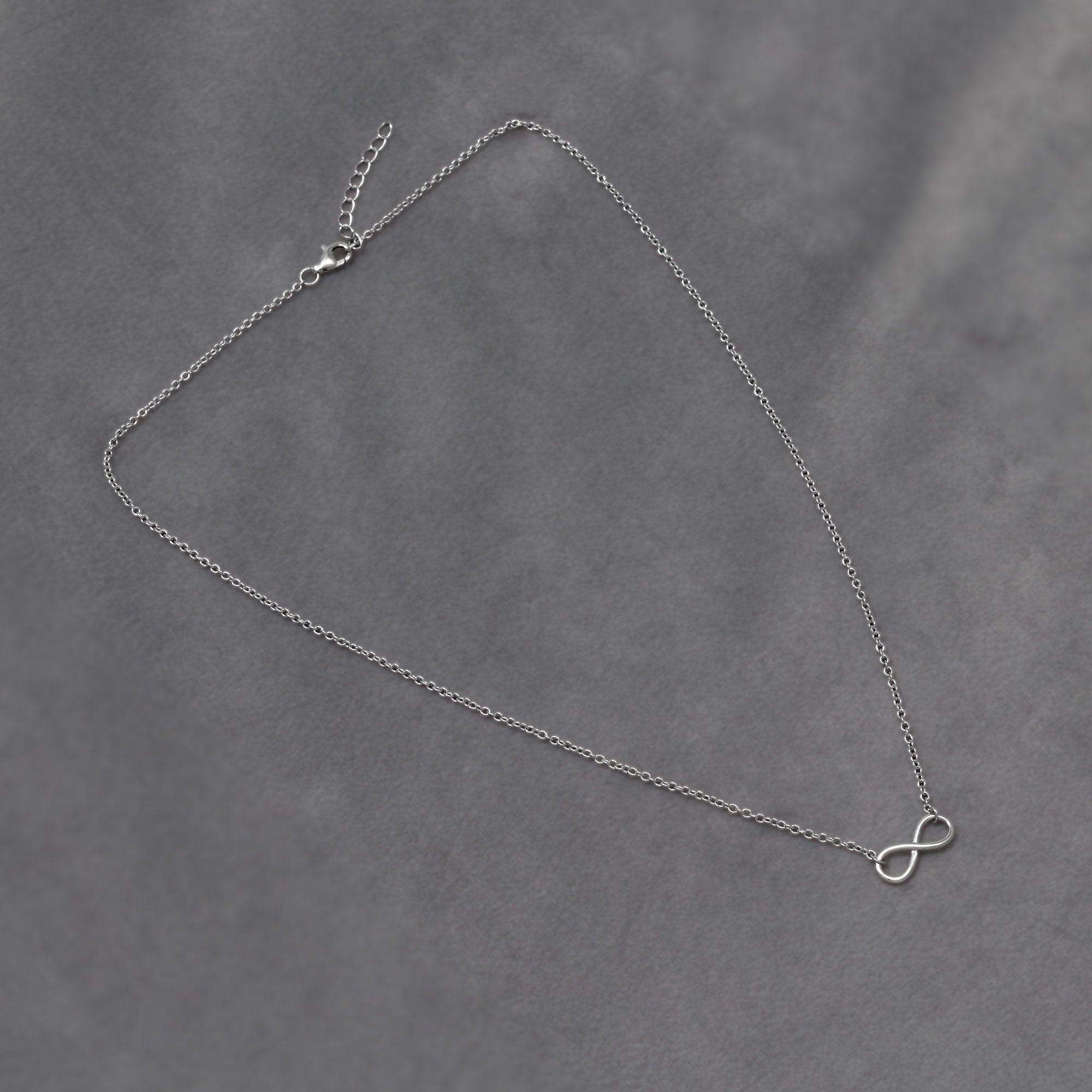A delicate sterling silver necklace featuring a simple infinity symbol pendant on a fine adjustable chain, embodying elegant and timeless design. Placed on a grey velvet cloth.