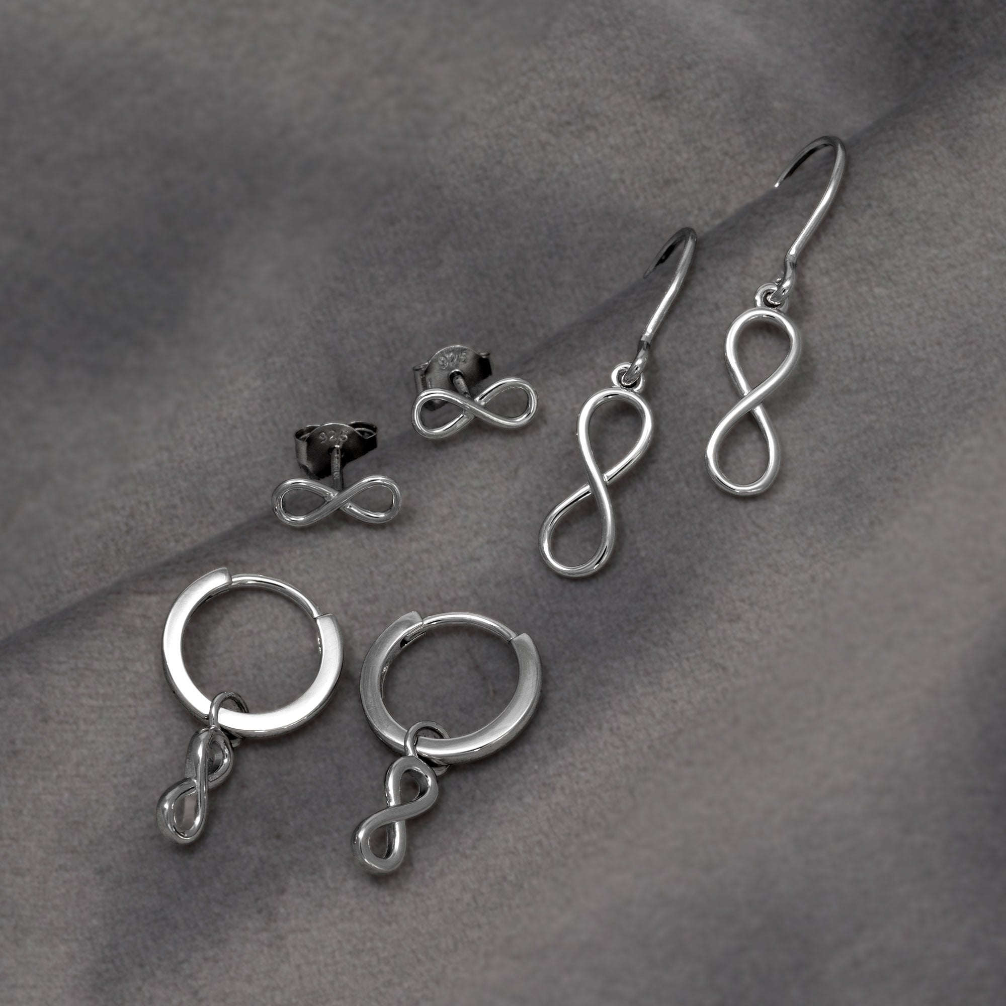 A collection of sterling silver stud and drop earrings shaped as smooth infinity symbols, embodying elegant and contemporary silver jewellery design. Placed on a grey velvet cloth.