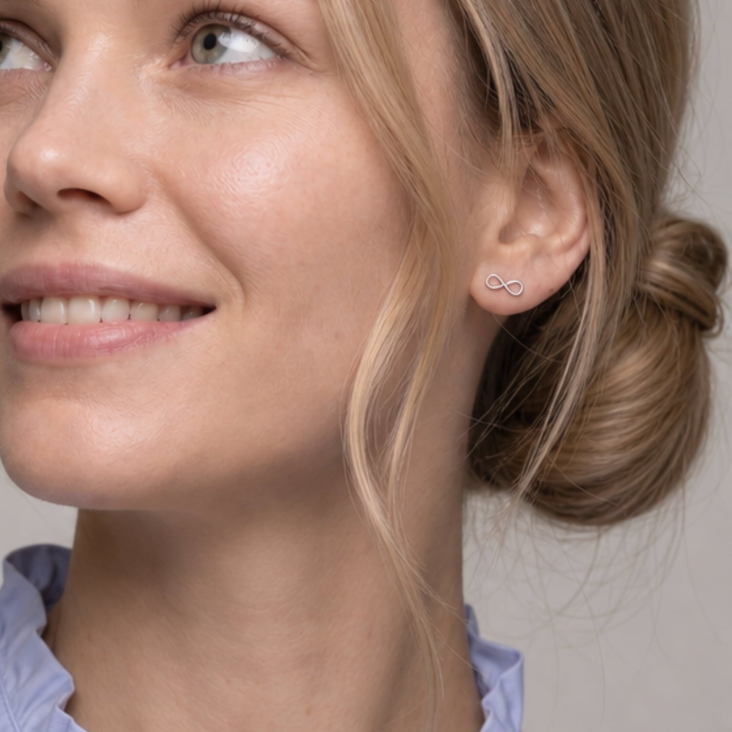 Close-up of a woman's ear wearing a delicate sterling silver infinity stud earring, showcasing the minimalist and sculptural design of contemporary silver jewellery.