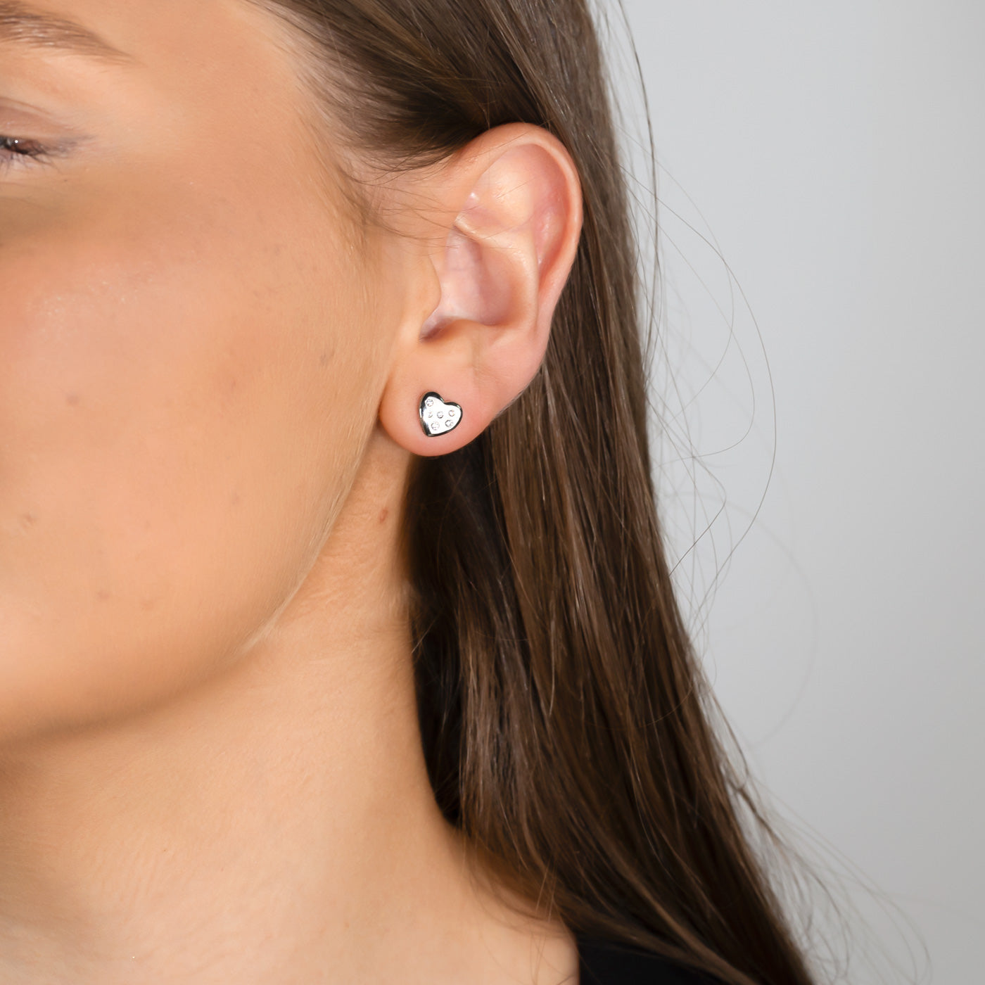 Close-up of a woman wearing sterling silver heart-shaped stud earrings embellished with scattered stone details, showcasing a minimalist and elegant design.