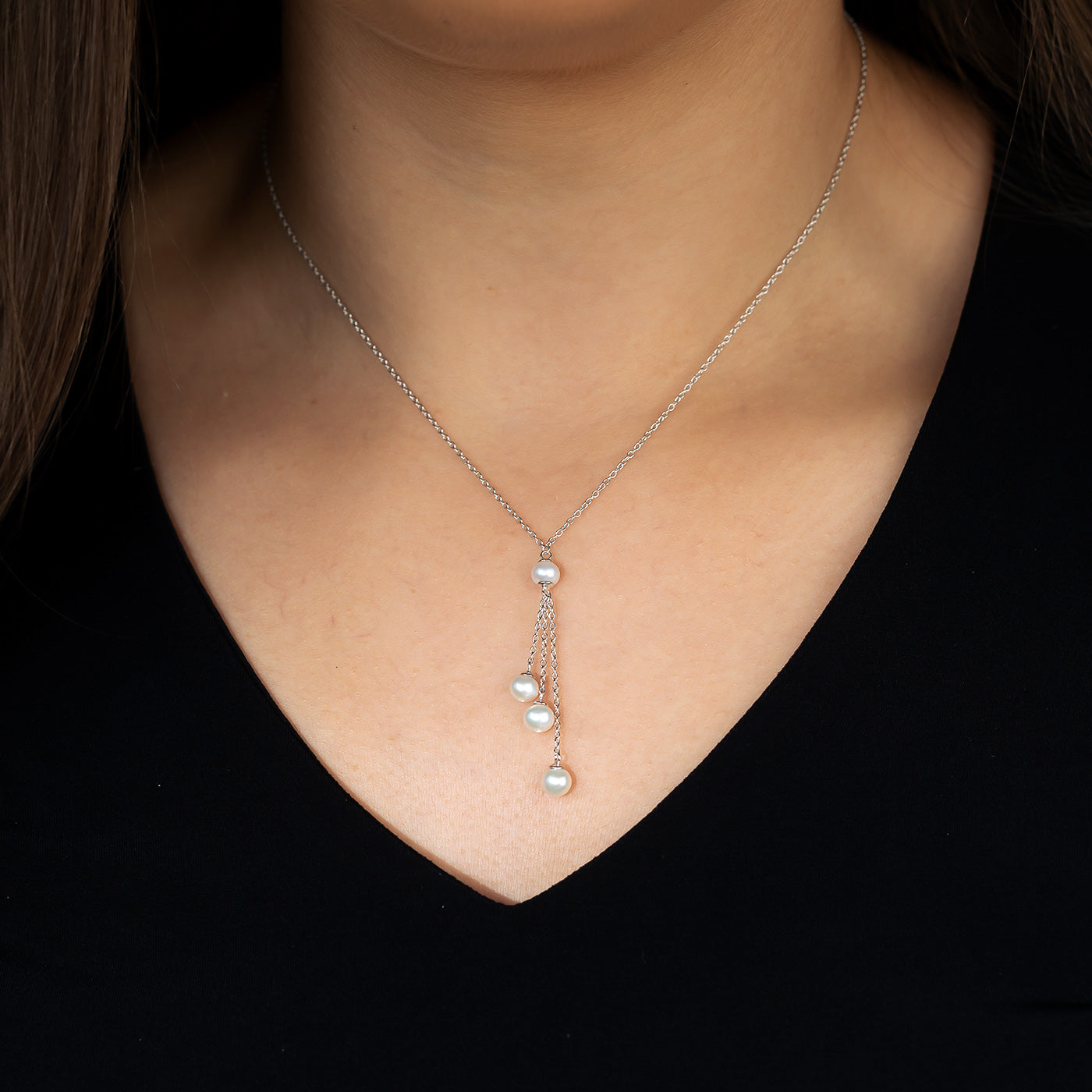 A sterling silver necklace with an adjustable chain featuring a delicate pearl and chain tassel detail, worn against a black V-neck top.