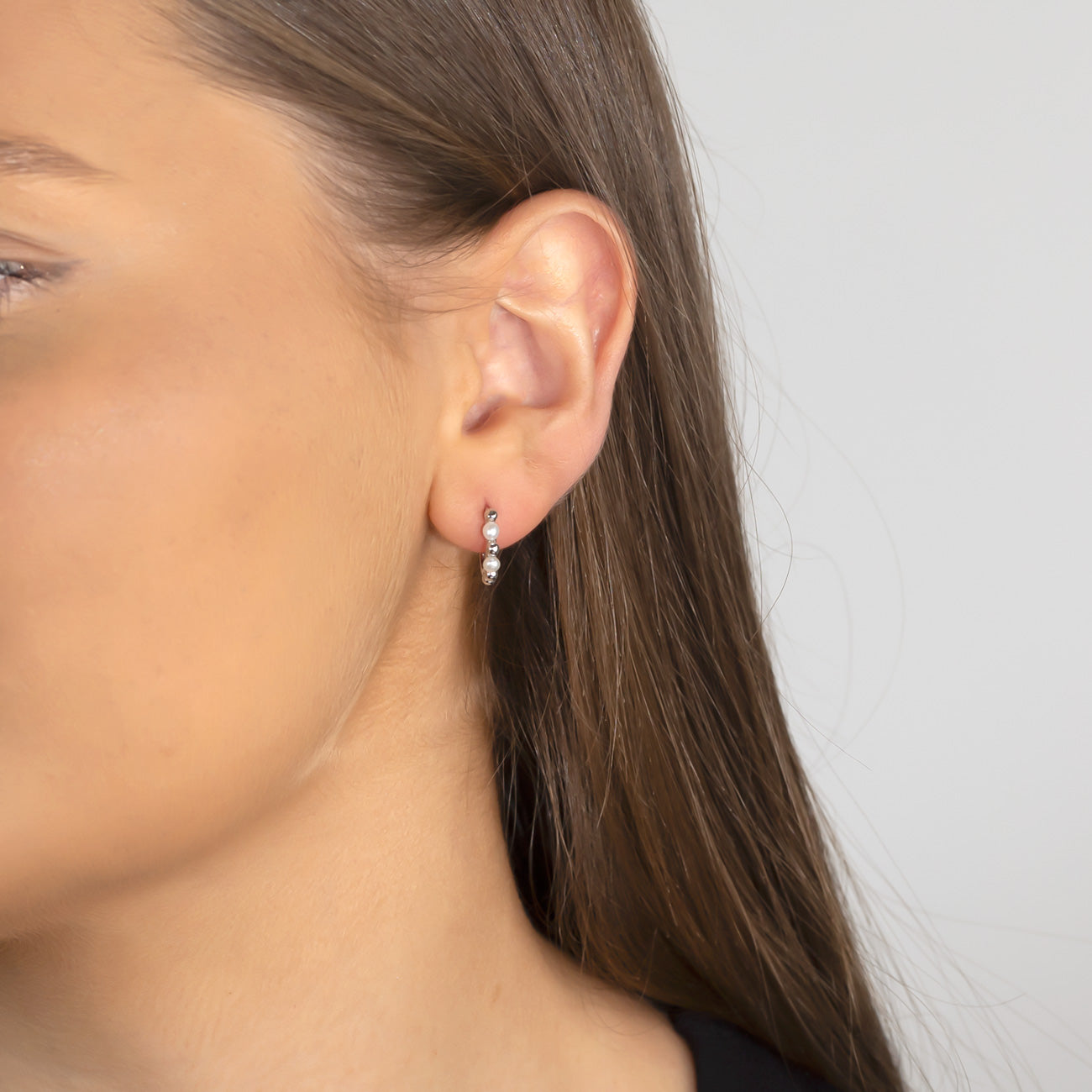 A close-up of a woman's ear wearing a sterling silver hinge hoop earring featuring a small pearl and polished silver bead, highlighting sleek and elegant silver jewellery design.