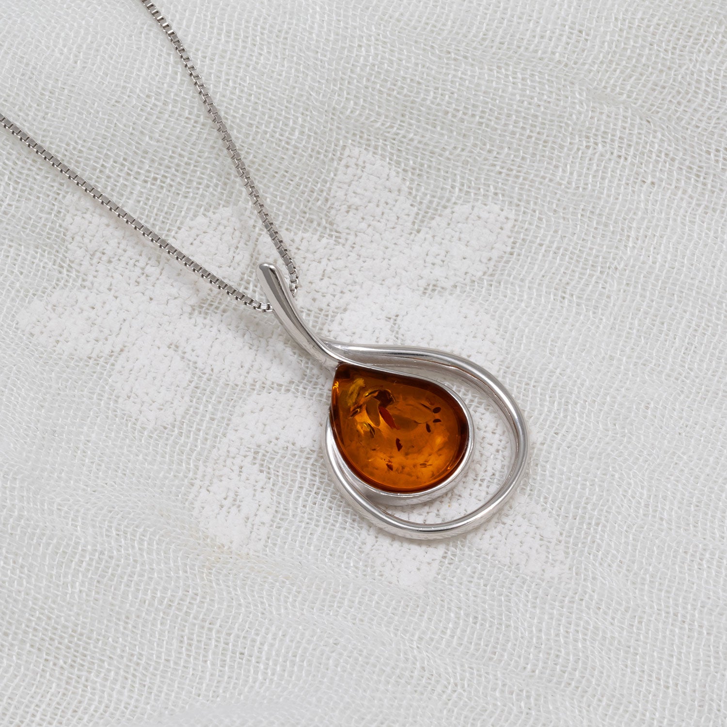 Elegant sterling silver pendant featuring a curling teardrop design with a warm amber gemstone, exemplifying refined British craftsmanship by Azendi.