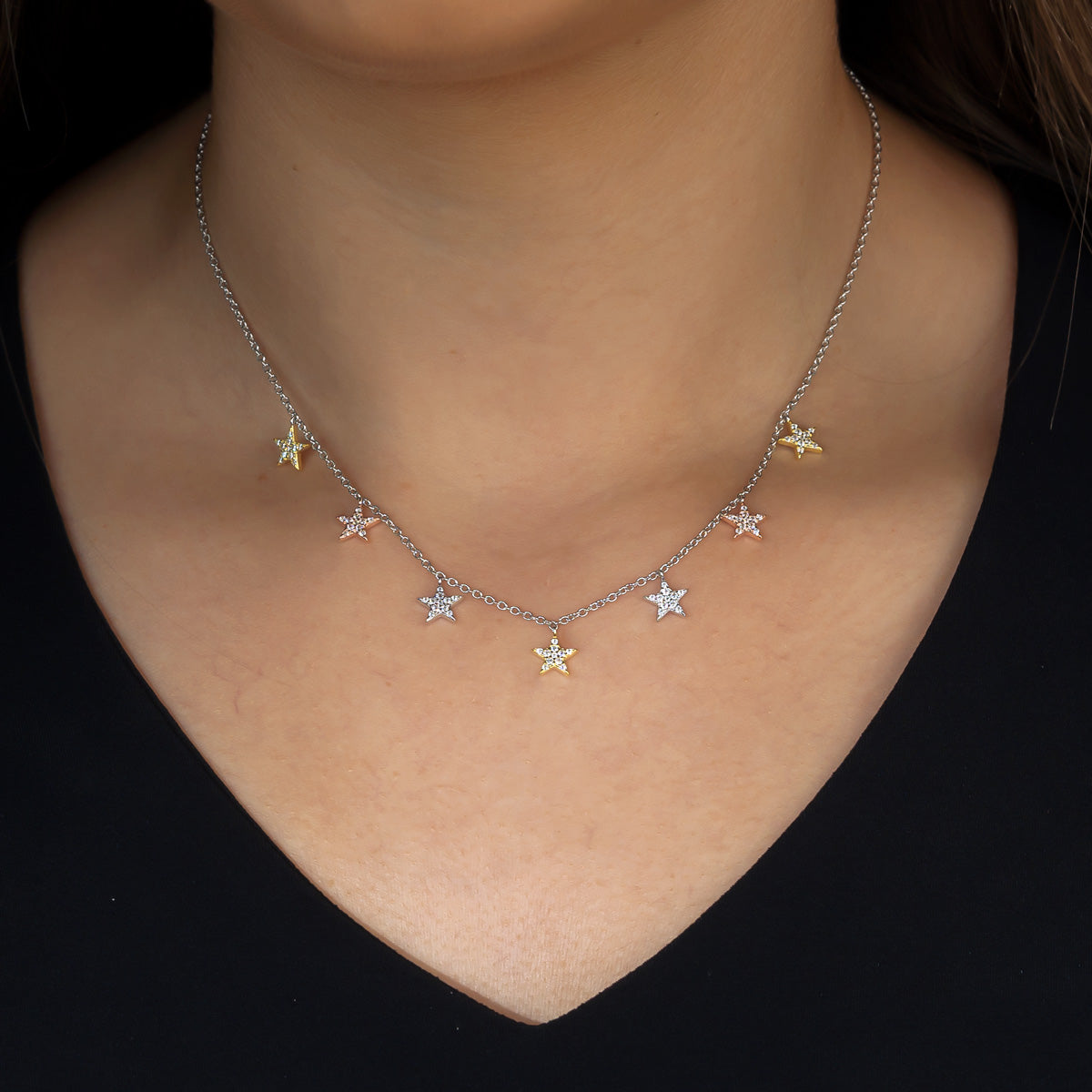 Delicate mixed vermeil necklace featuring seven star-shaped charms embellished with pavé stones, suspended from a fine sterling silver chain on a neutral skin tone background.