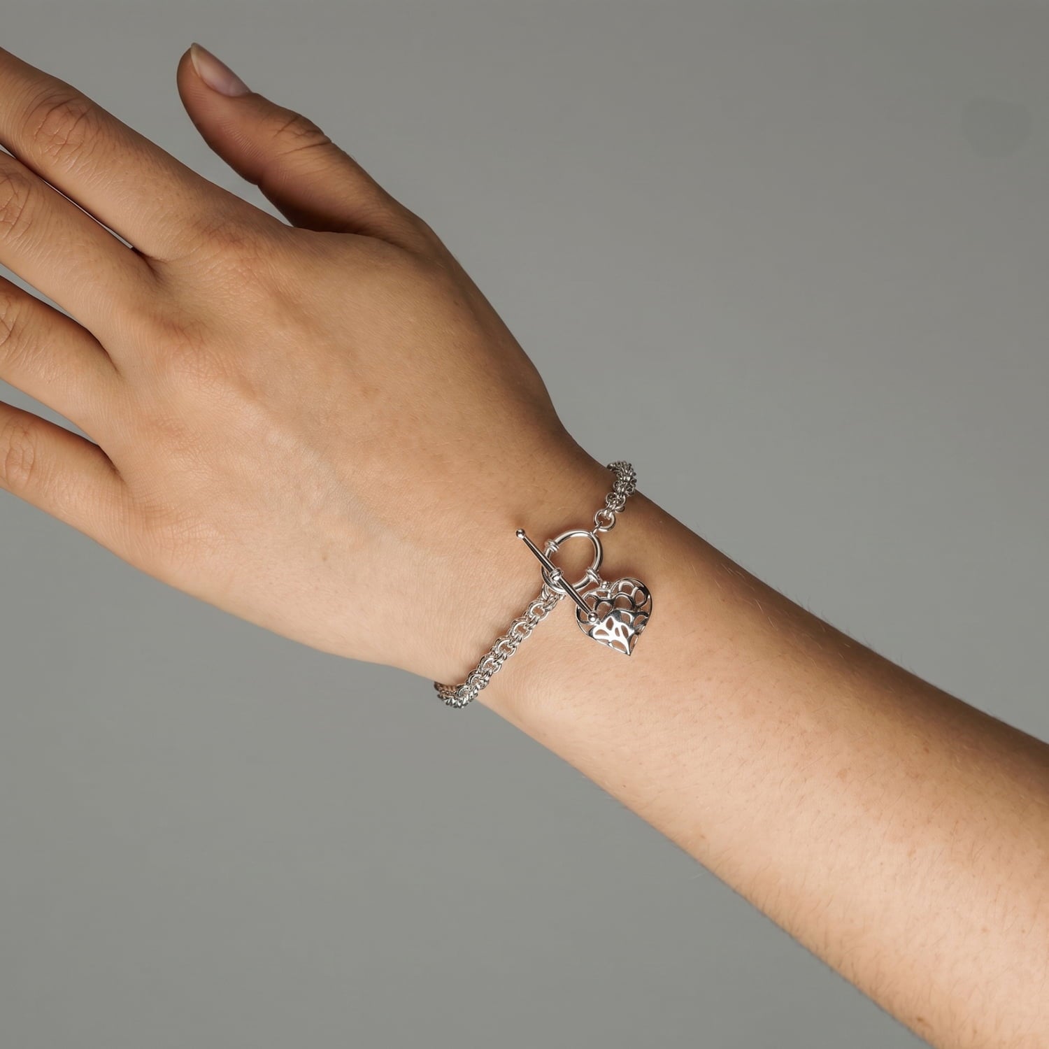 Sterling silver bracelet featuring a sculptural Yorkshire-inspired hanging heart charm and T-bar clasp, worn on the wrist showcasing fine silver jewellery craftsmanship.