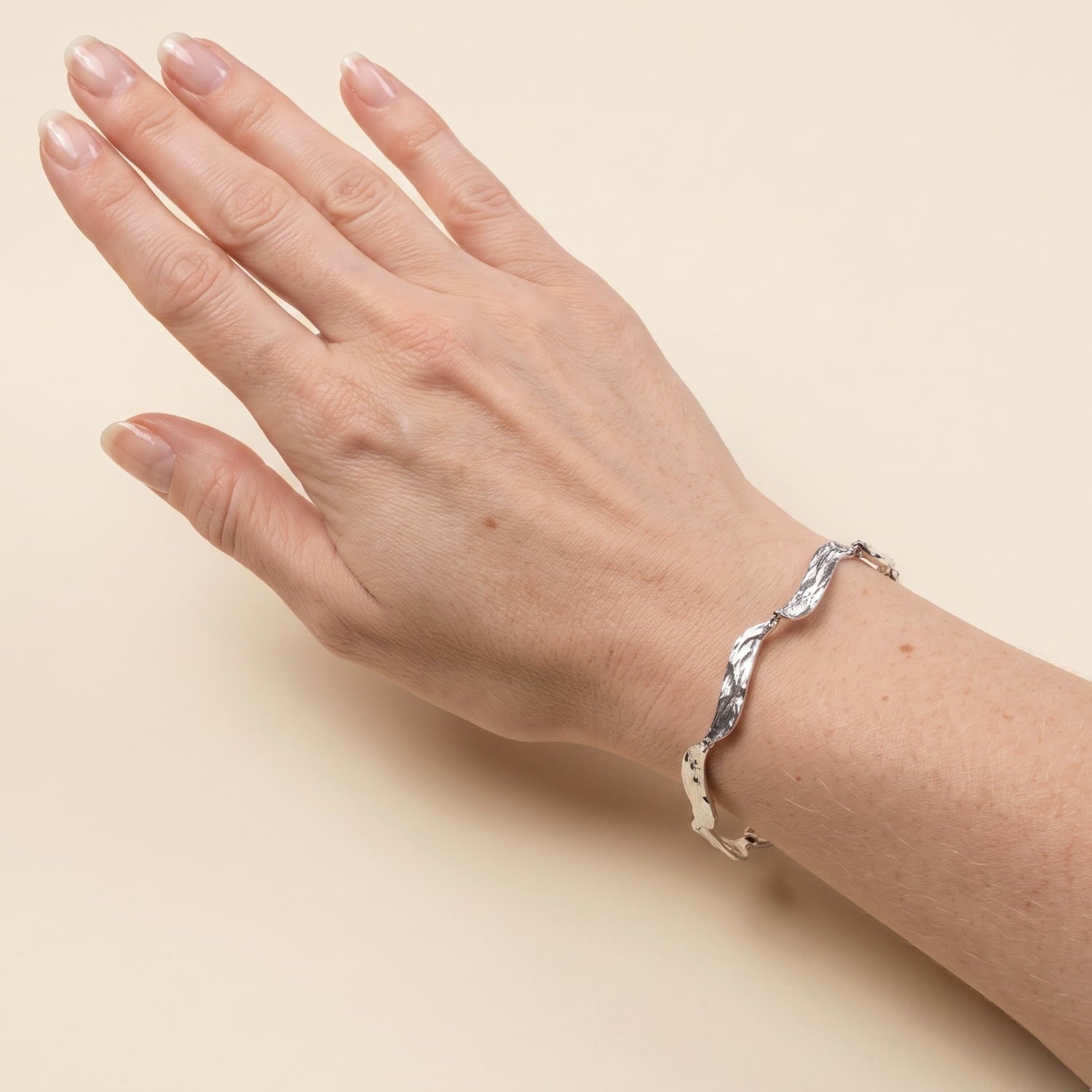 Model wears sterling silver bracelet composed of wavy sculptural, textured links connected by small rings.