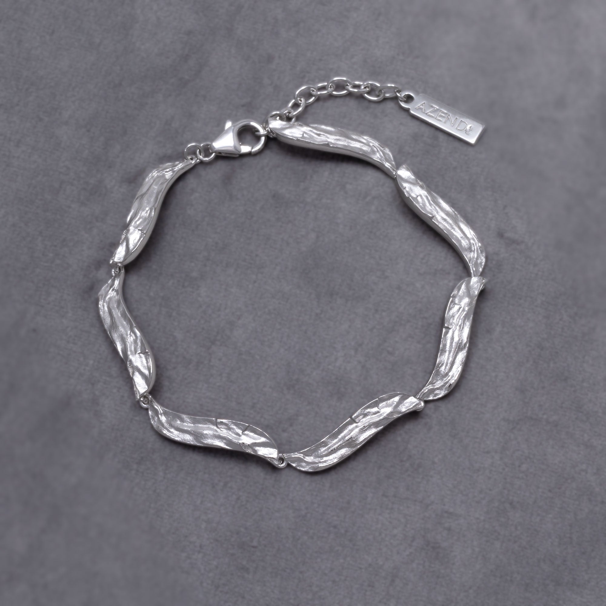 Sculptural sterling silver bracelet featuring textured, undulating links with adjustable chain closures, showcasing contemporary British silver jewellery design. placed on a grey velvet cloth.