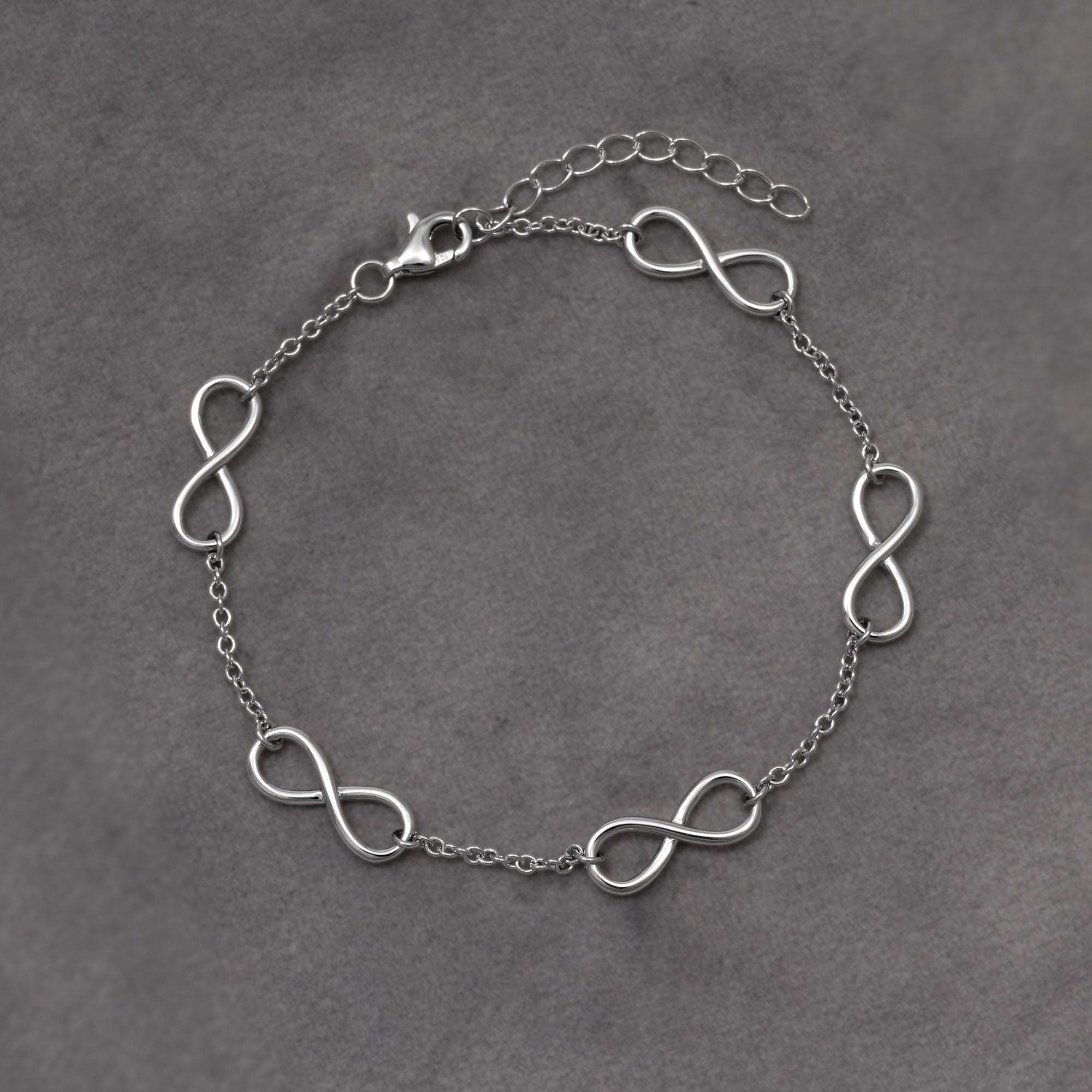 Delicate sterling silver bracelet featuring multiple interconnected infinity symbols on a fine chain with an adjustable clasp for versatile wear. Placed on a grey cloth.