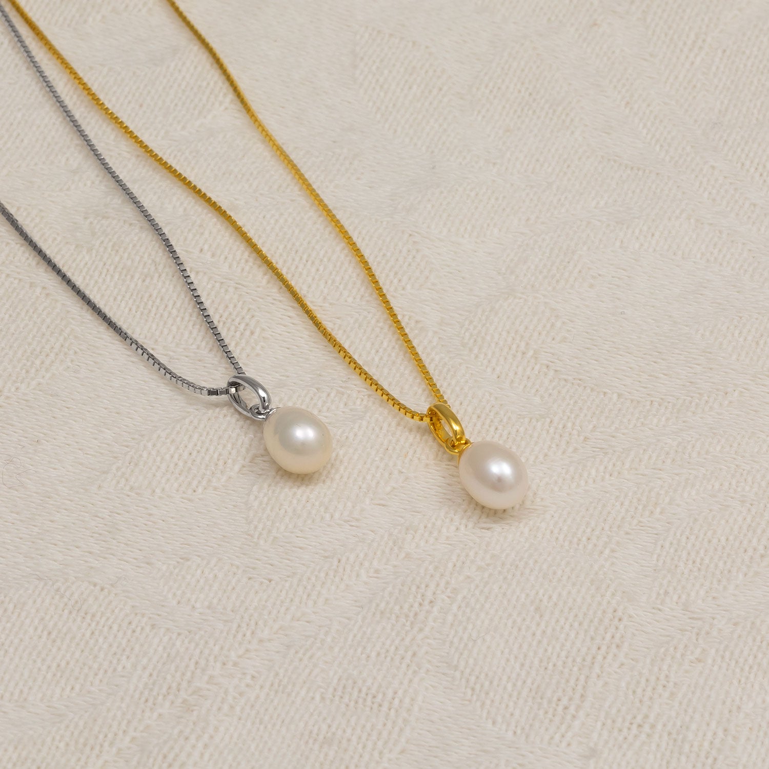 Two delicate necklaces displayed on a soft fabric surface, each featuring a single teardrop-shaped freshwater pearl pendant, one on a gold vermeil chain and the other on a sterling silver chain.
