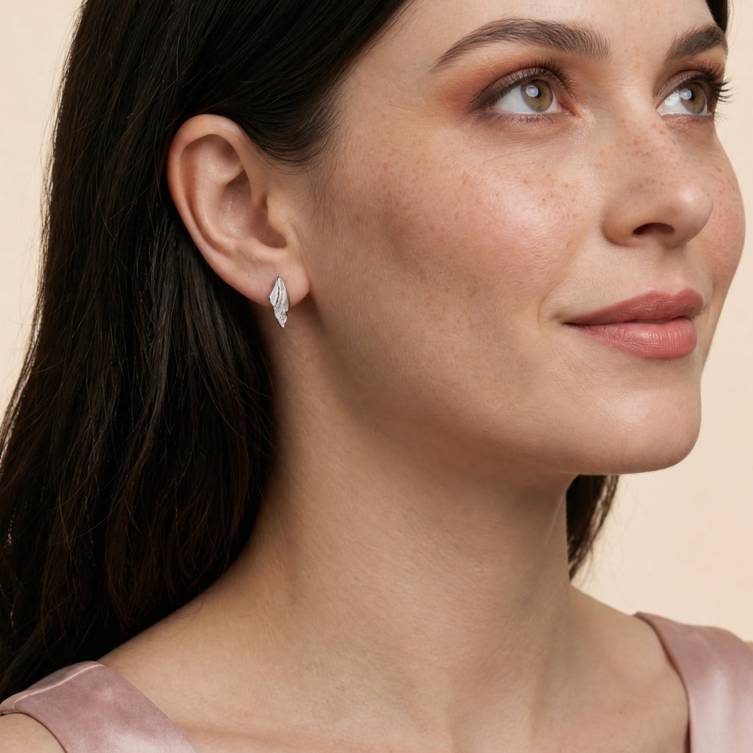 A model wears a pair of sterling silver stud earrings featuring a curved design with textured and polished surfaces, showcasing sculptural elegance in contemporary silver jewellery.