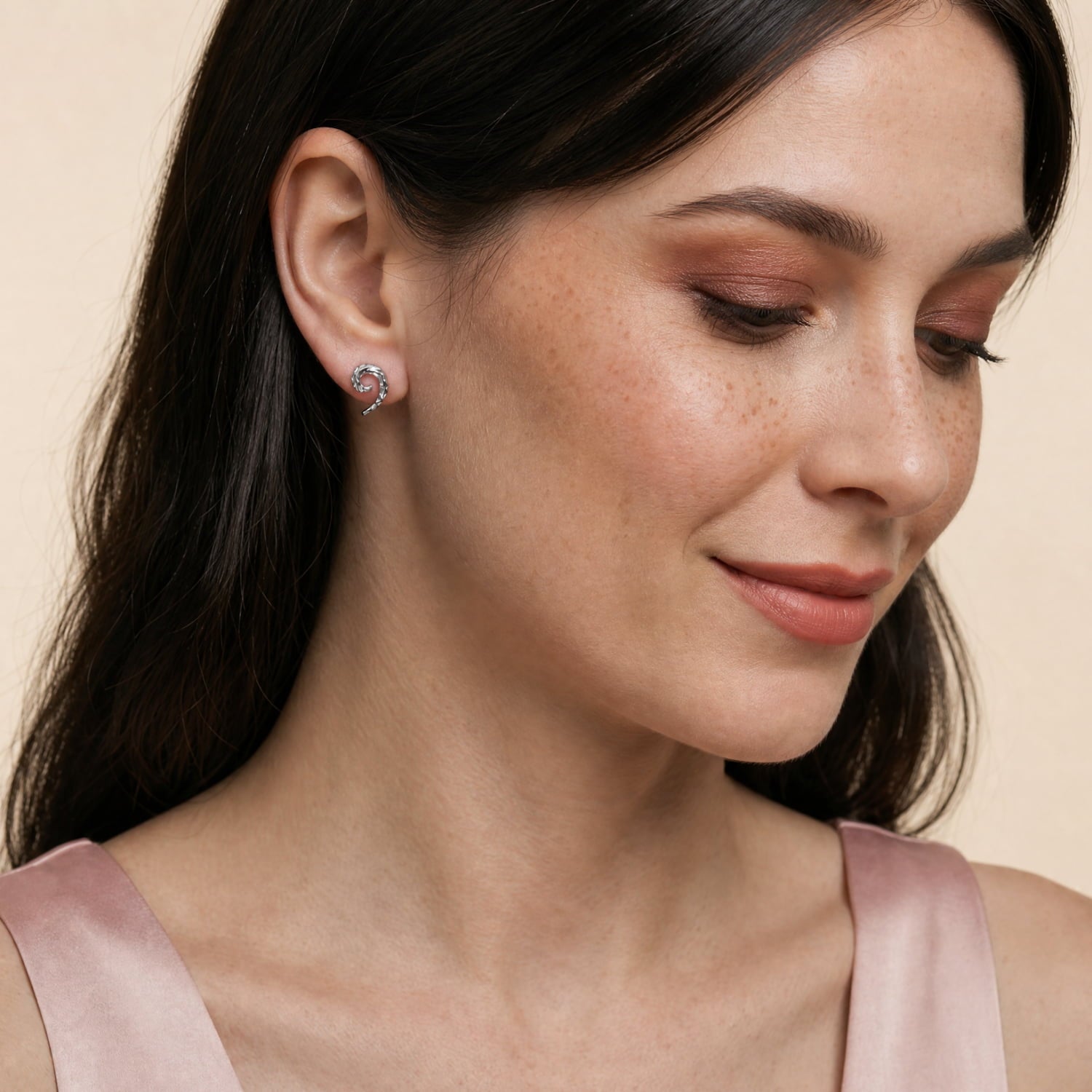 A close-up of a model wearing textured sterling silver stud earrings featuring a sculptural curling horn shape with a hammered finish, exemplifying refined contemporary silver jewellery.