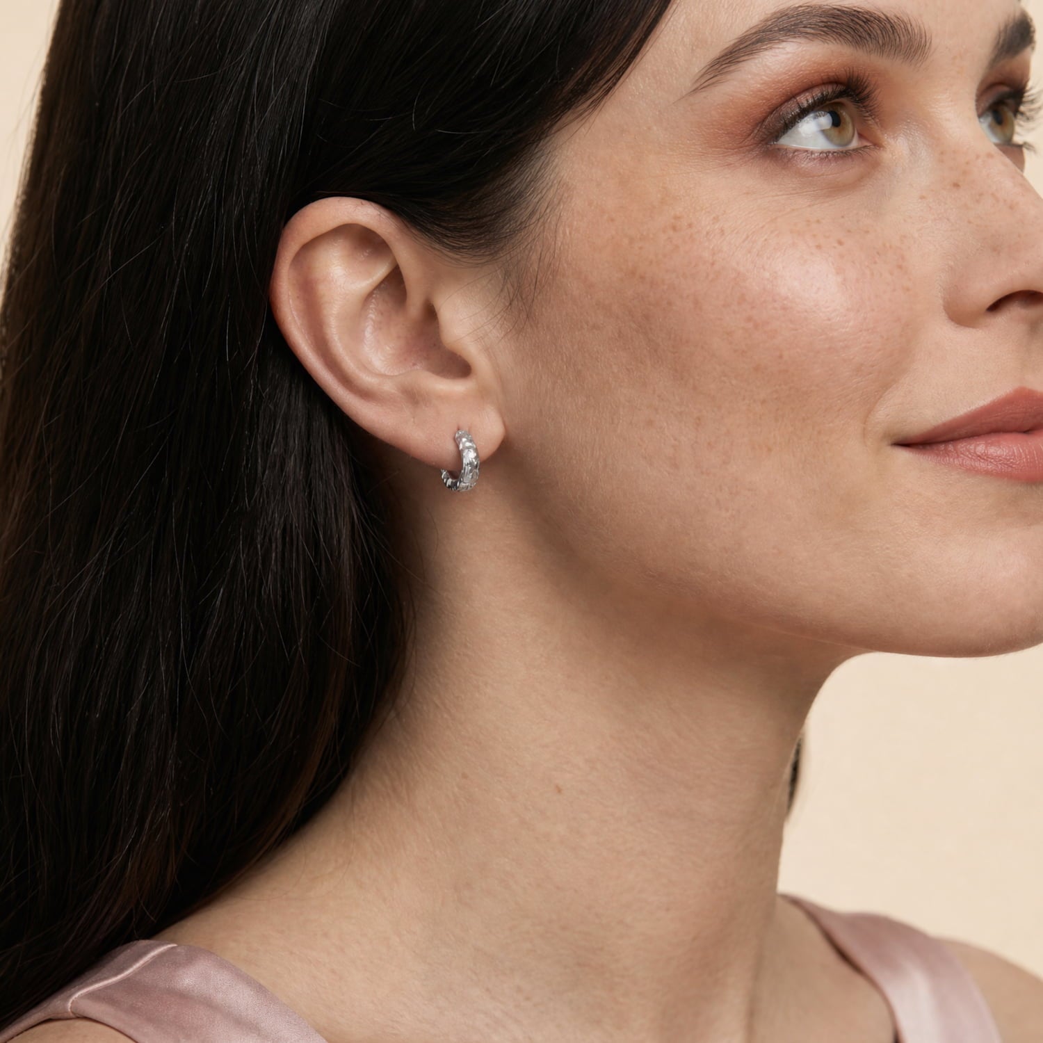 Model wears a pair of textured sterling silver half hoop earrings with a sculptural, hammered finish, offering a contemporary and elegant design in fine silver jewellery by Azendi.