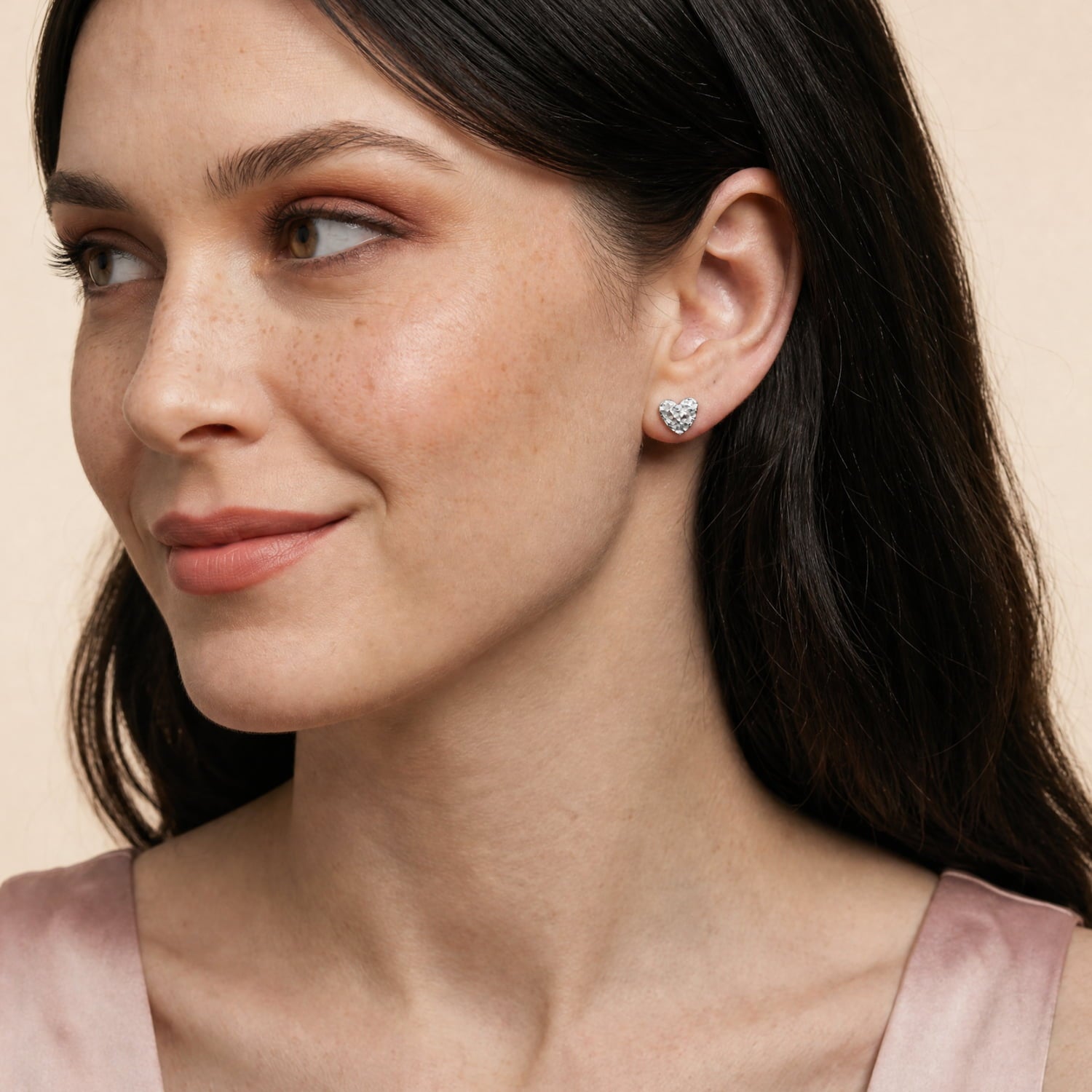 A model wears textured sterling silver heart shaped stud earrings featuring an organic, textured surface.