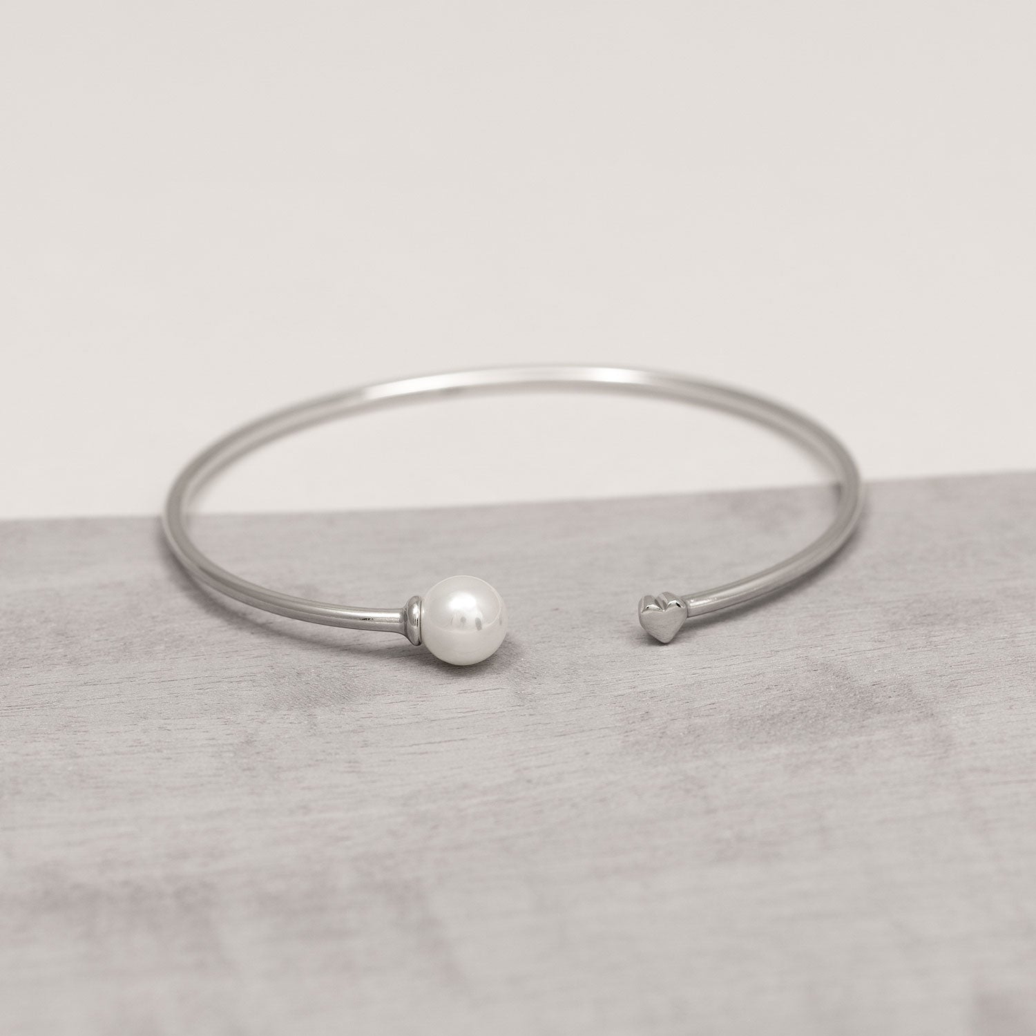 Sterling silver open cuff bracelet featuring a smooth shell pearl on one end and a delicate heart detail on the other, offering a refined and contemporary design.