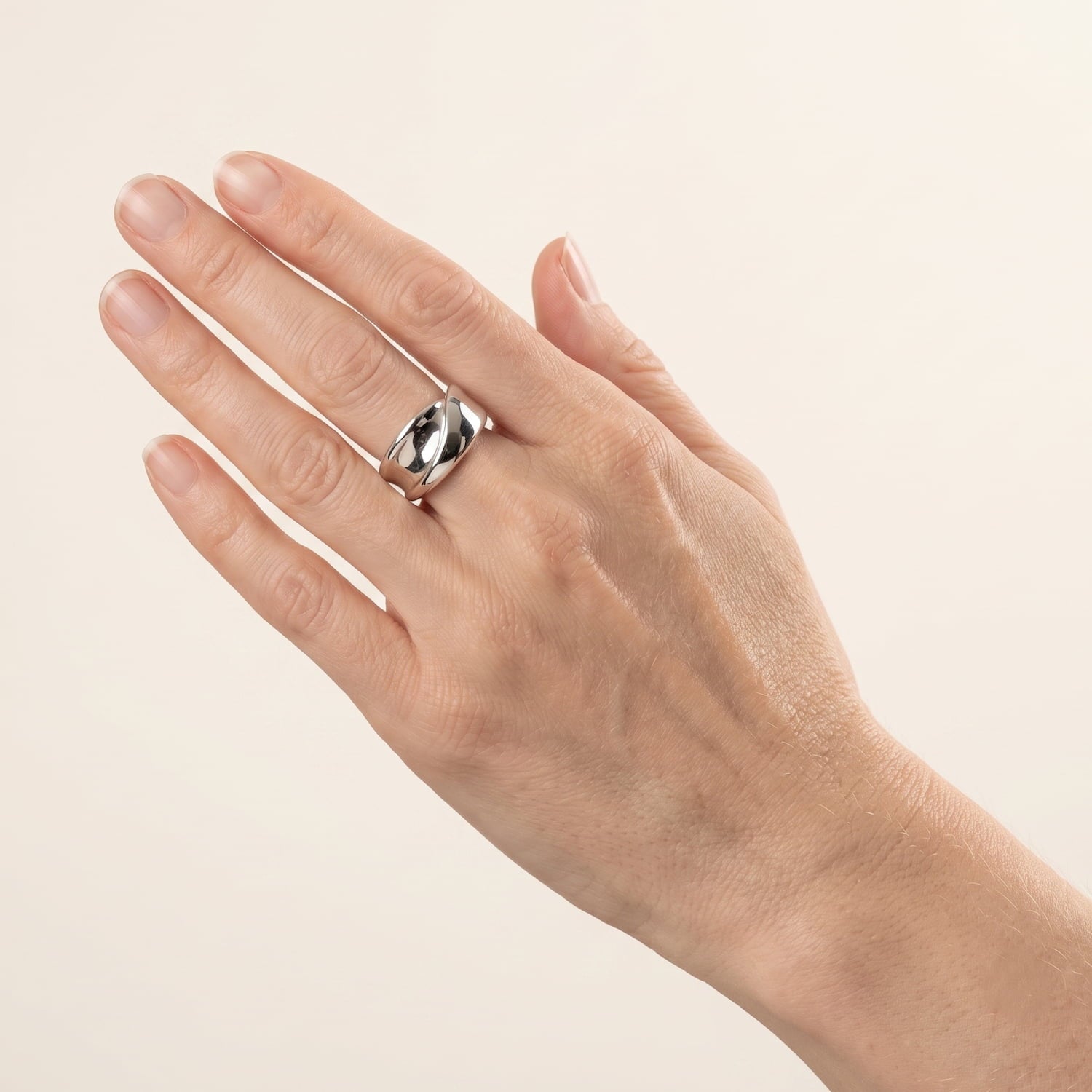 Model wears a polished sterling silver ring featuring a sculptural twisting ribbon design with smooth, reflective surfaces in a contemporary style.