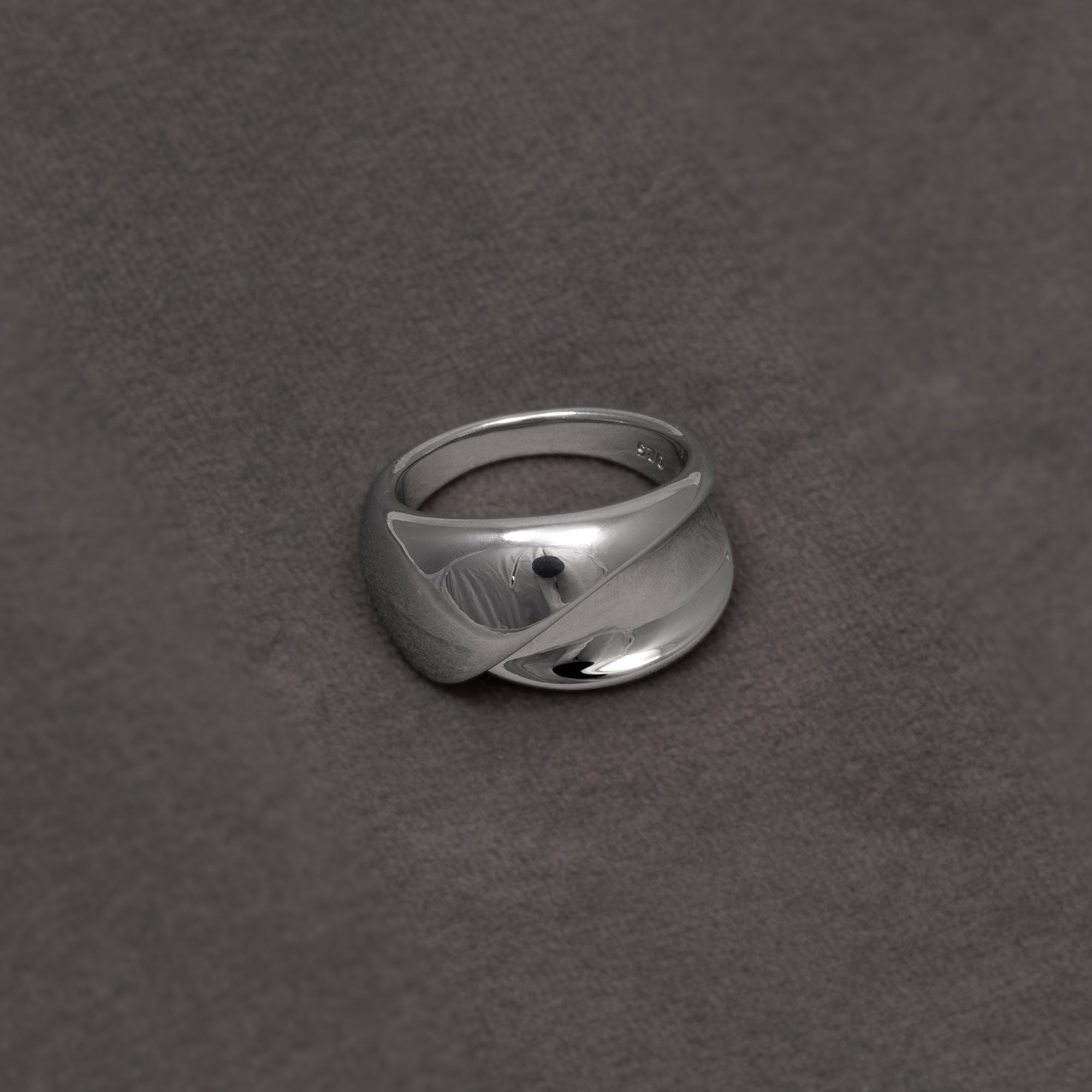 Polished sterling silver ring featuring a sculptural twisting ribbon design with smooth, reflective surfaces in a contemporary style. Placed on a grey velvet cloth.