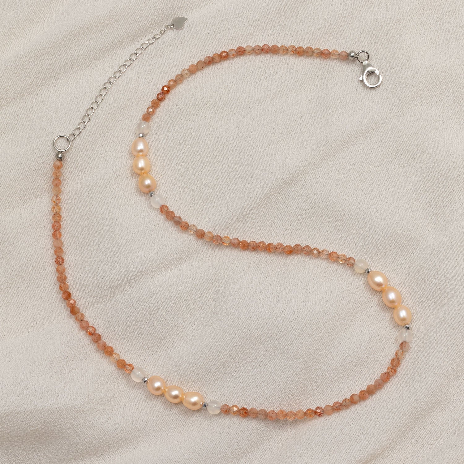 Delicate sterling silver necklace featuring faceted sunstone beads interspersed with clusters of lustrous freshwater pearls on a soft beige fabric background.