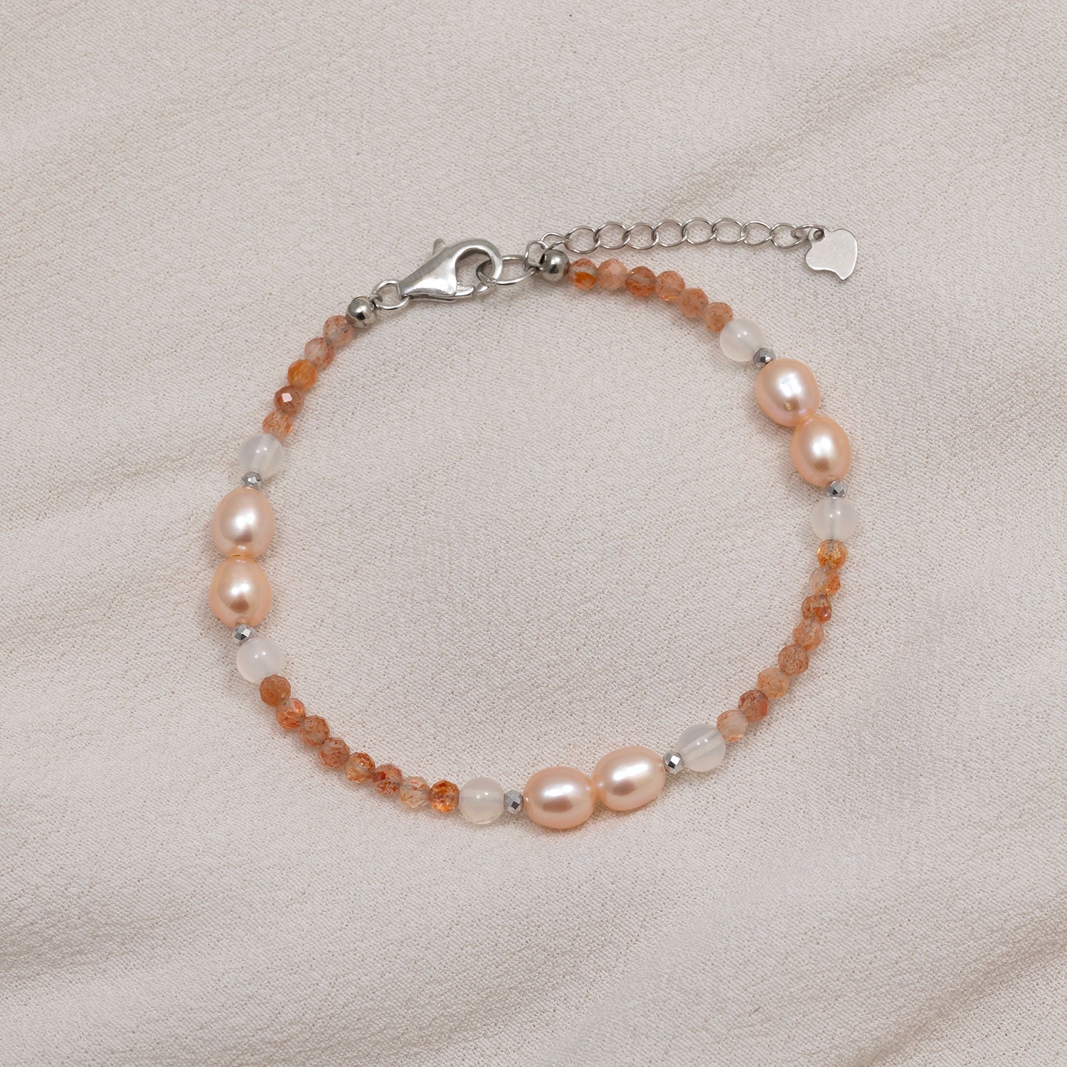 Delicate sterling silver bracelet featuring warm sunstone beads and lustrous freshwater pearls, designed with an adjustable chain for a refined, elegant look.