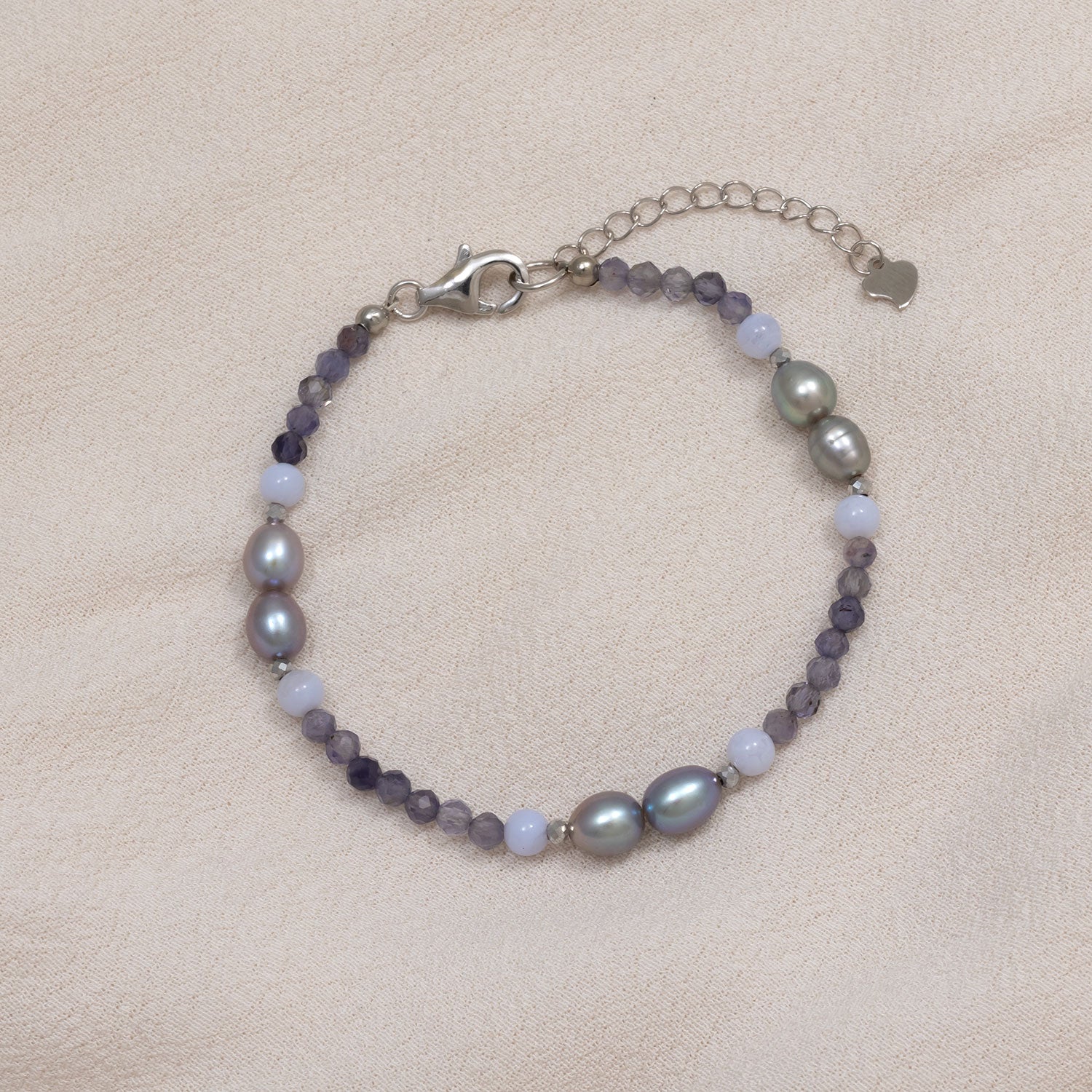 Delicate sterling silver bracelet featuring smooth freshwater pearls and faceted iolite beads with an adjustable chain and heart-shaped charm on a soft beige background.