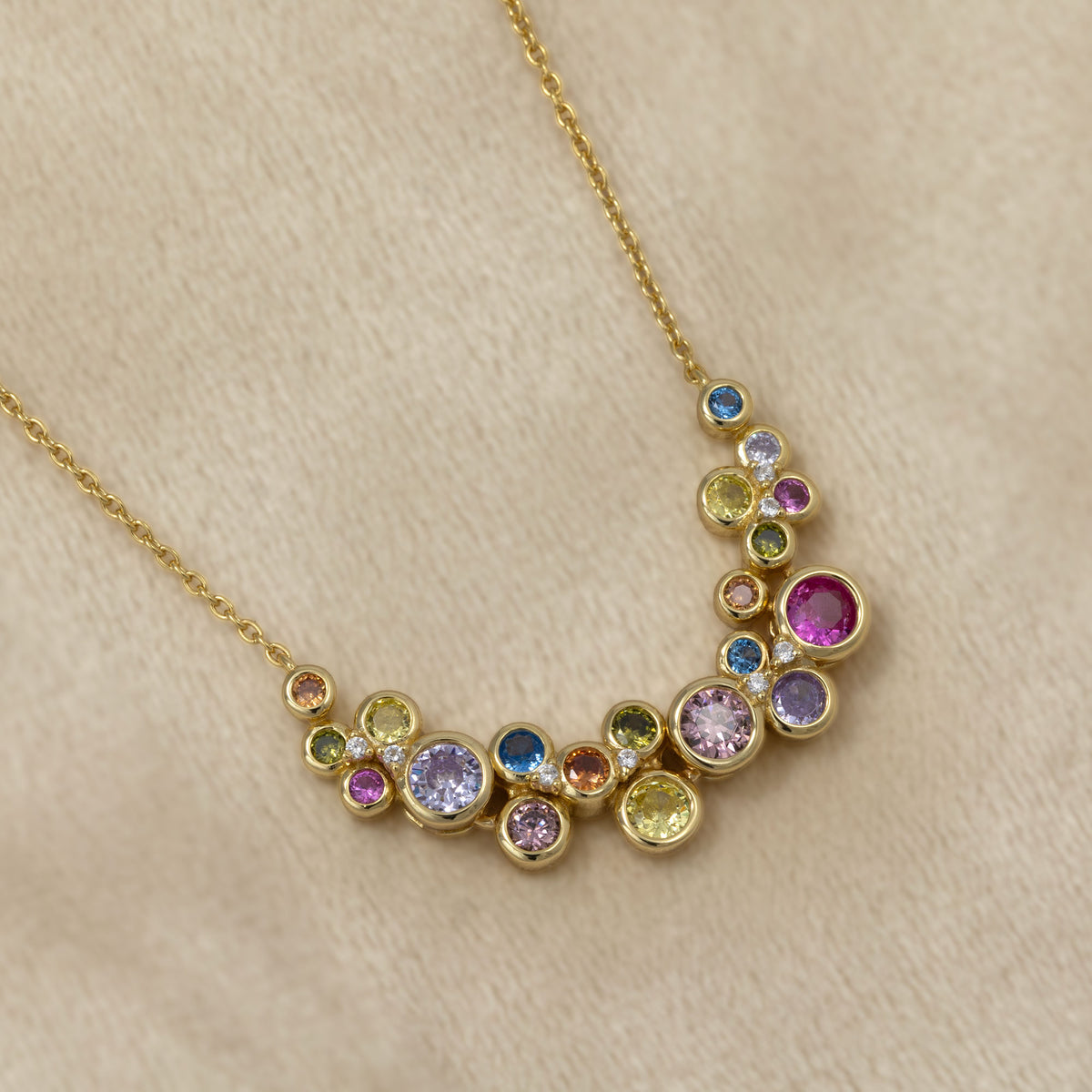 Gold vermeil necklace featuring a cluster of colourful bubble-like gemstones in varied hues for a vibrant, sculptural look. Placed on a cream velvet cloth.