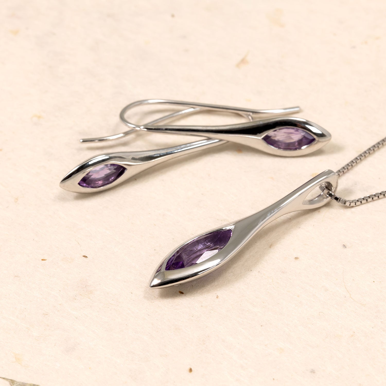 Elegant sterling silver drop earrings and matching pendant, each featuring a marquise-cut amethyst gemstone set within smooth, sculptural silver frames for a refined jewellery statement.