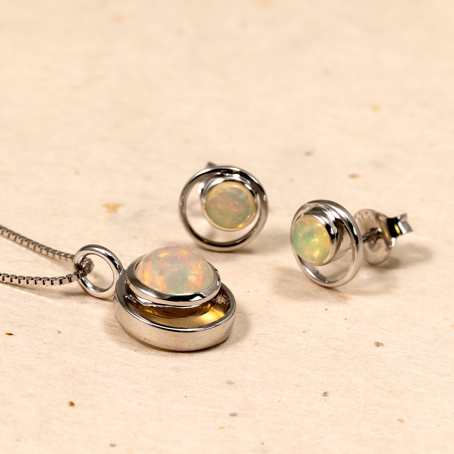 Pair of sterling silver stud earrings featuring round opal gemstones set within open circular frames, styled with a matching pendant necklace showcasing a layered opal centerpiece.