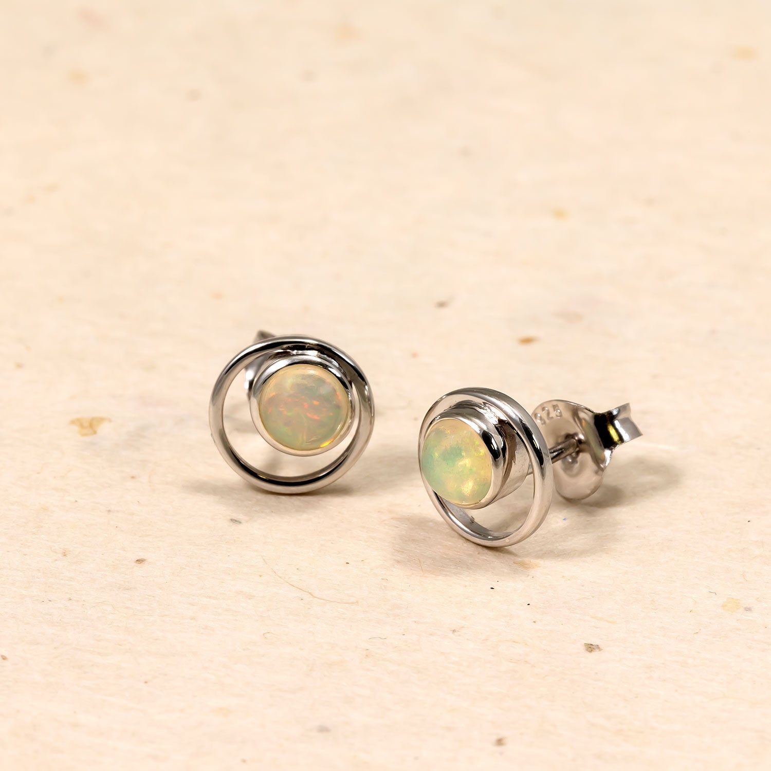 Pair of sterling silver stud earrings featuring circular open frames with central opal gemstones, showcasing a modern, sculptural design with subtle iridescent tones.