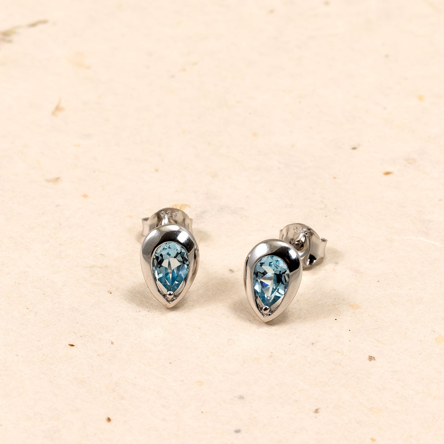 Pair of sterling silver stud earrings featuring sky blue topaz gemstones cut in a teardrop shape, showcasing a sleek and sculptural design by an award-winning British jeweller.
