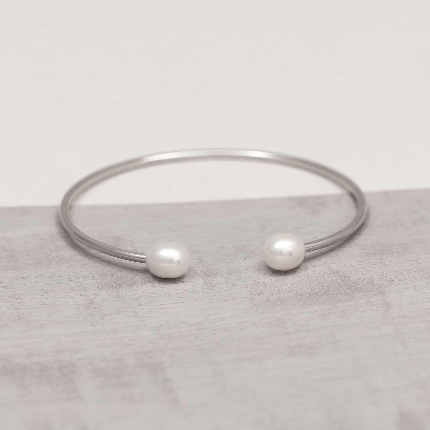 Open-ended sterling silver cuff bracelet featuring two smooth freshwater pearls at each tip, showcasing a contemporary and sculptural design aesthetic.
