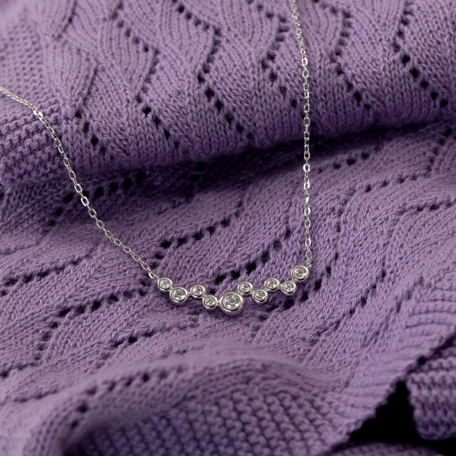 Delicate sterling silver necklace featuring a cluster of sparkling cubic zirconia stones set in polished bezels, displayed on textured purple knit fabric.