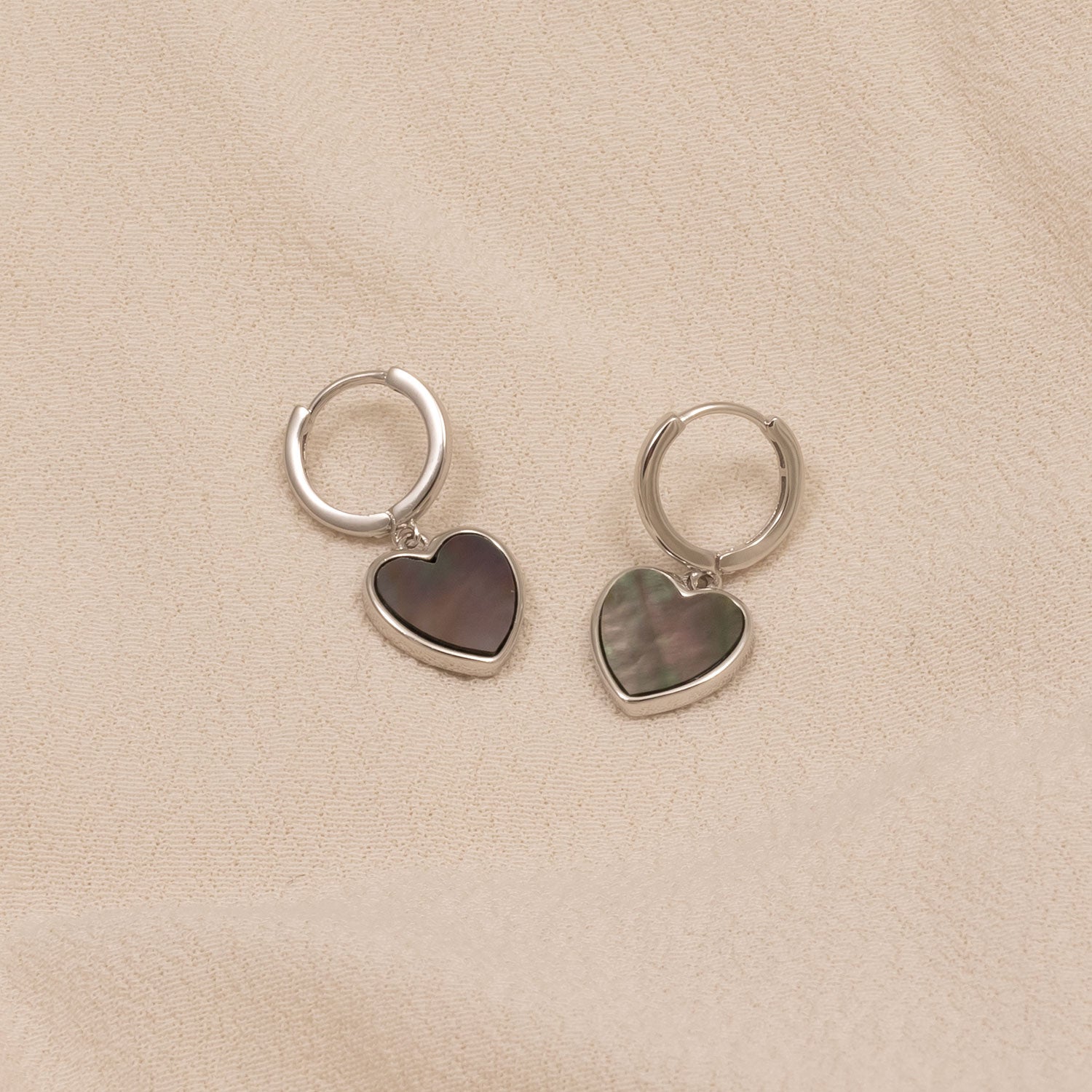 Pair of sterling silver hoop earrings featuring heart-shaped grey mother of pearl charms, showcasing a sleek and contemporary design with subtle iridescent tones.