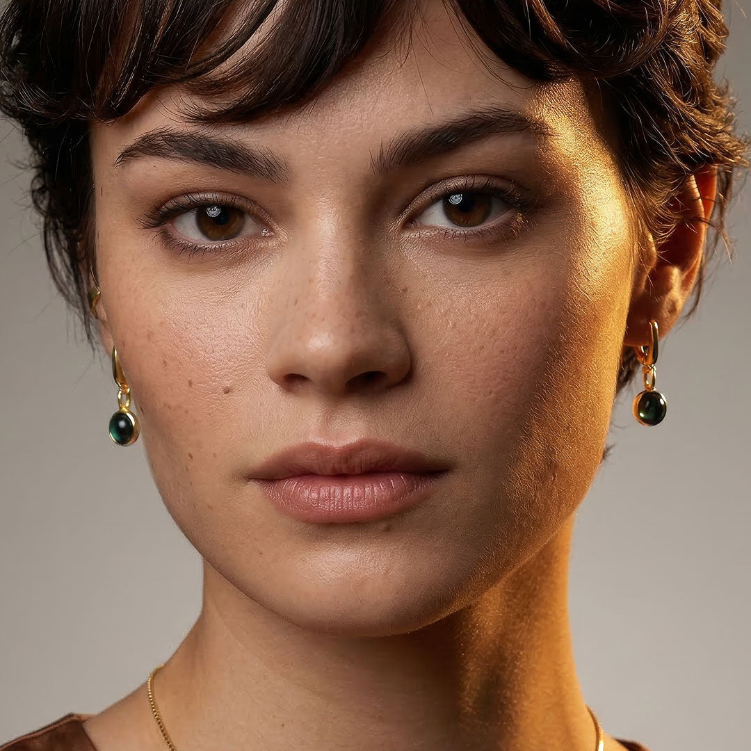Close-up of a model wearing gold vermeil drop earrings featuring polished malachite stones, showcasing elegant and sculptural sterling silver jewellery by a British designer.