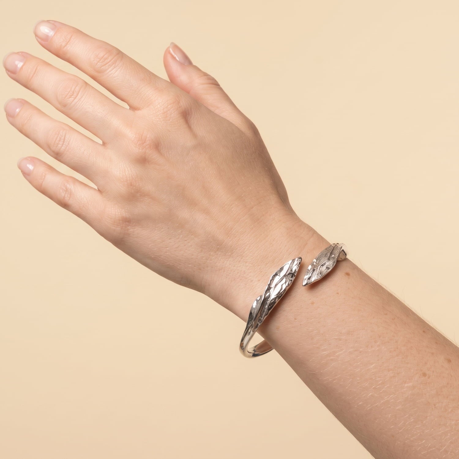 Model wears curved sterling silver hinged bangle featuring a textured and polished finish with sculptural leaf-shaped ends.
