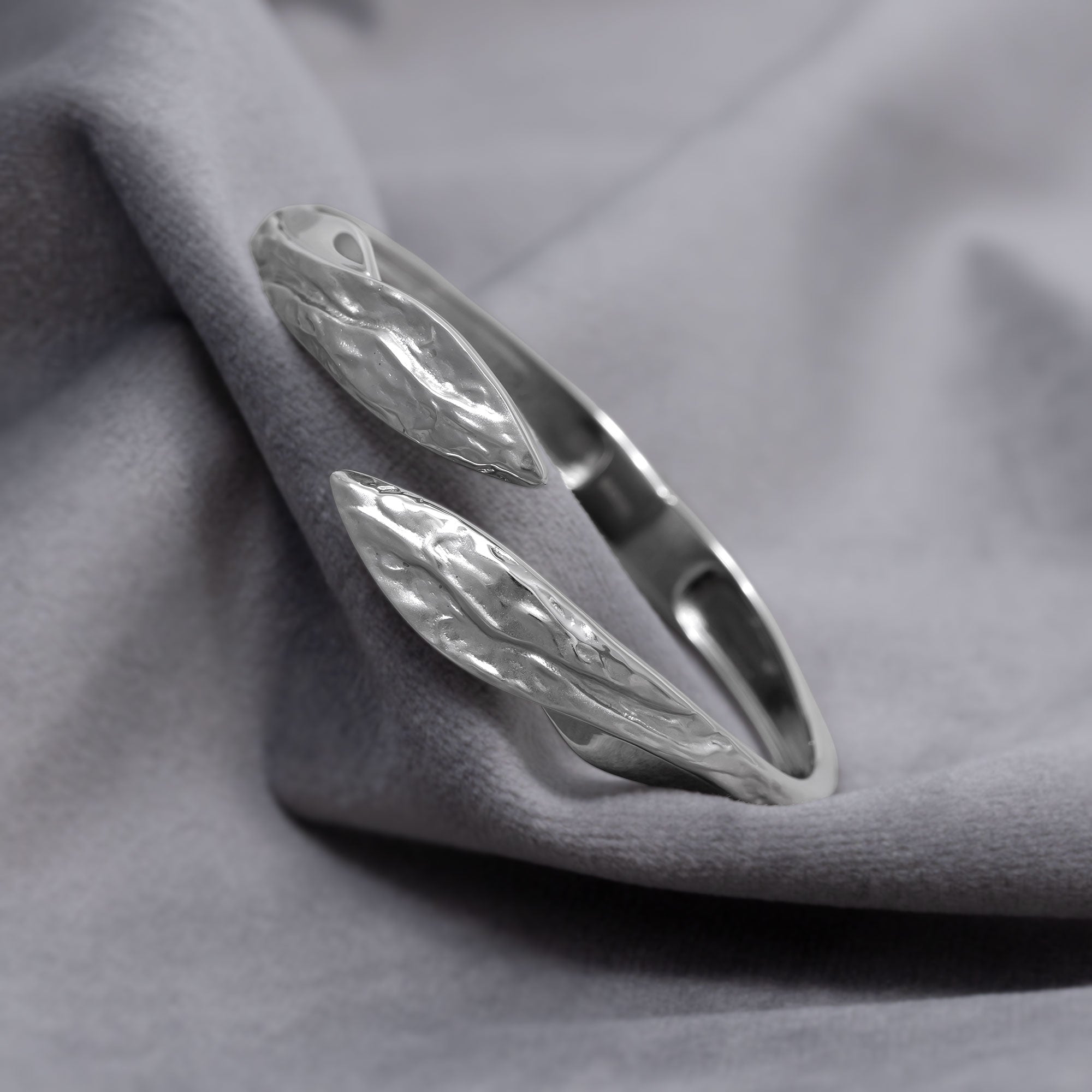 Curved sterling silver hinged bangle featuring a textured and polished finish with sculptural leaf-shaped ends, exemplifying refined contemporary silver jewellery by Azendi. Placed on a grey velvet cloth.