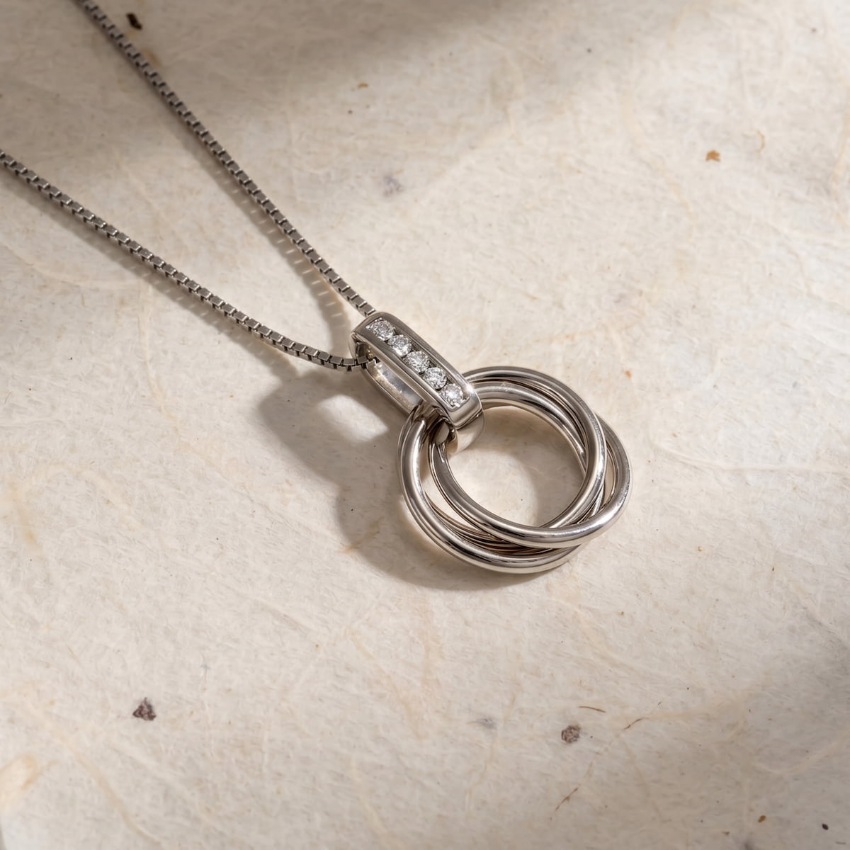 Sterling silver pendant featuring intertwined circular loops with a polished finish, accented by a row of sparkling lab-grown diamonds on the bail, suspended on a fine chain.