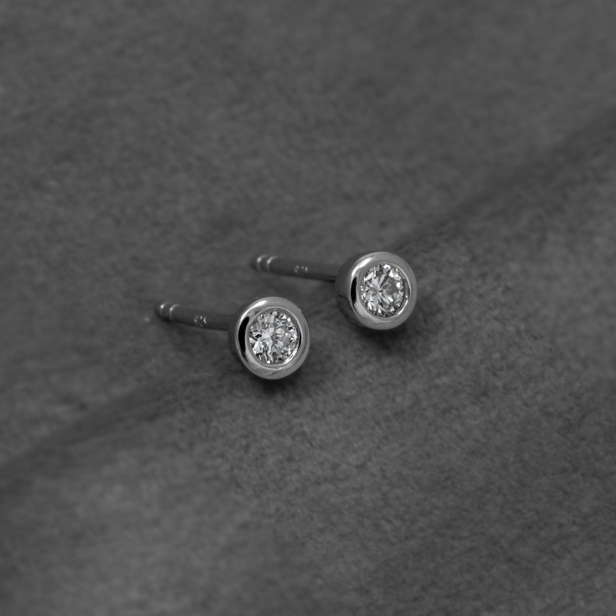 Pair of sterling silver solitaire stud earrings each set with a single 0.15 carat lab grown diamond in a smooth bezel setting for a refined, timeless look.